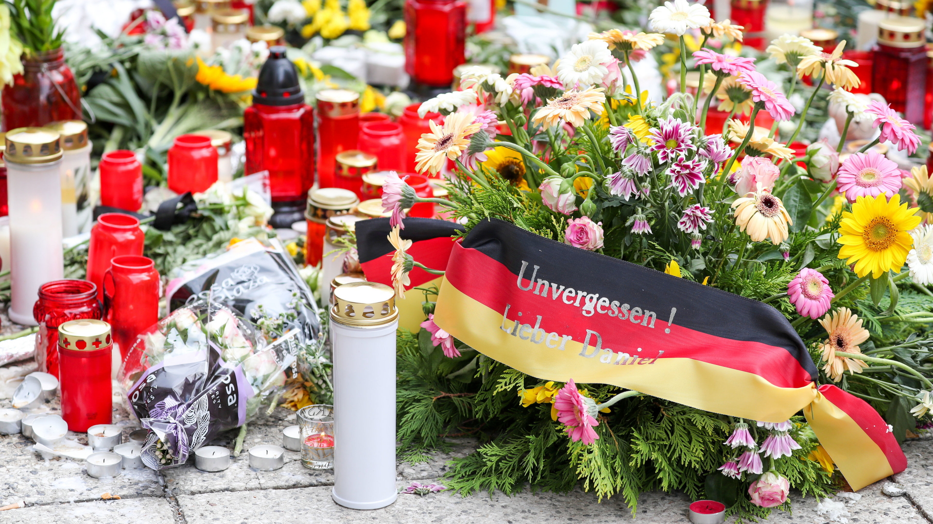 Kerzen und Blumen liegen auf einer Straße in Chemnitz, auf einer schwarz-rot-goldenen Binde steht: "Unvergessen! Lieber Daniel". | Bildquelle: dpa