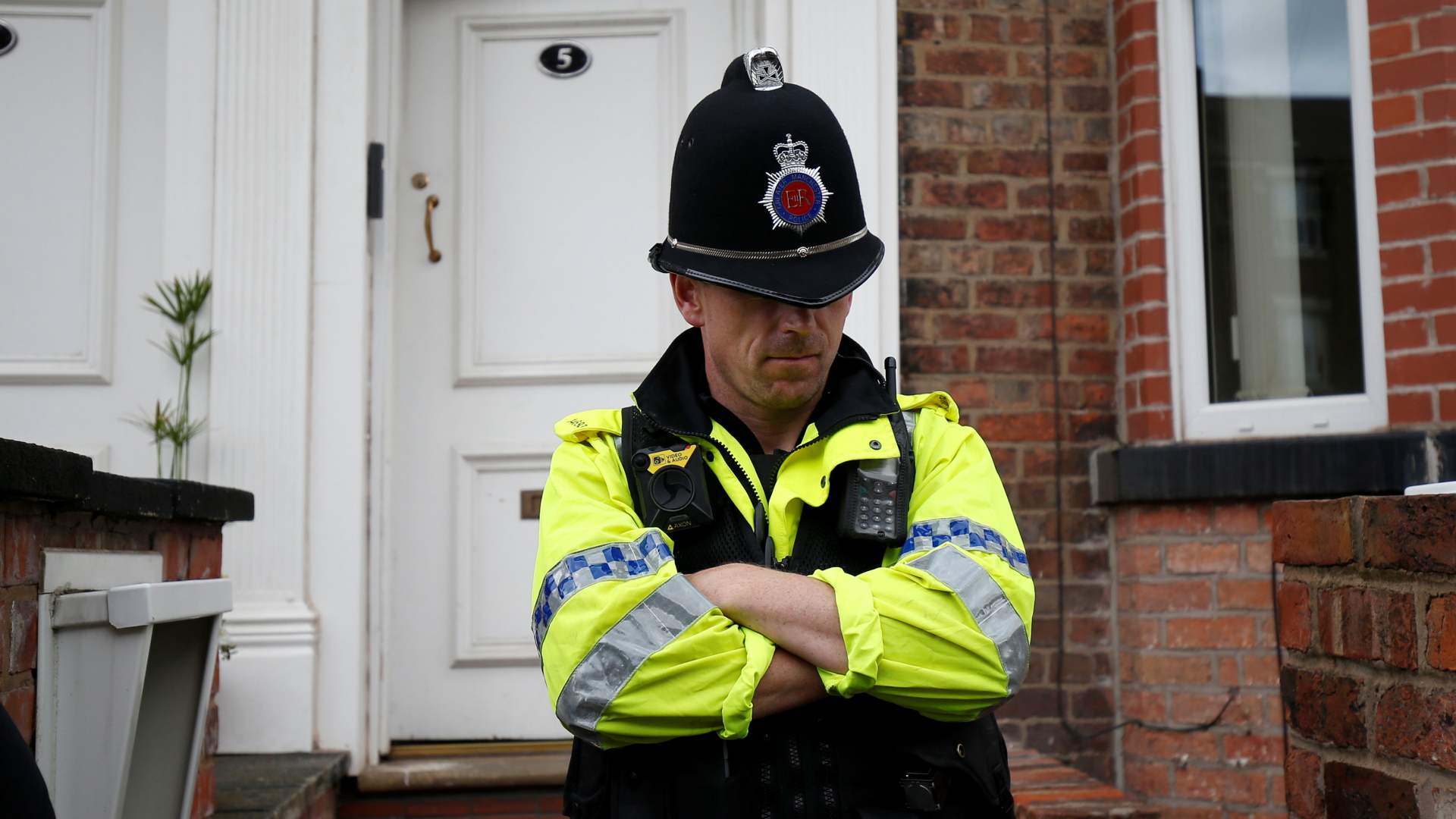 Ein britischer Polizist steht mit gesenktem Kopf vor einer Haustür. | Bildquelle: REUTERS