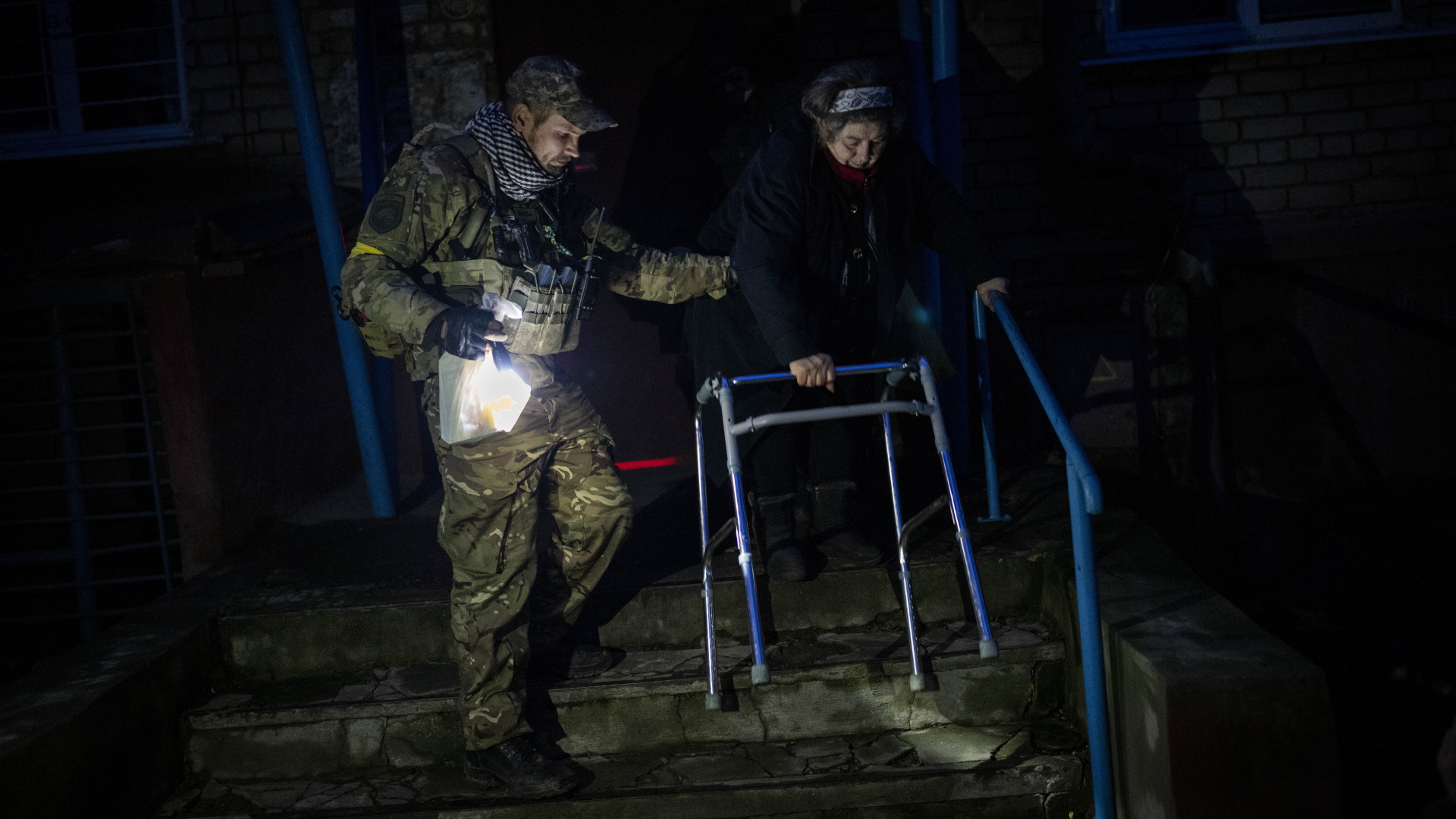 Ein Soldat hilft einer älteren Frau in Cherson mit einer Taschenlampe.