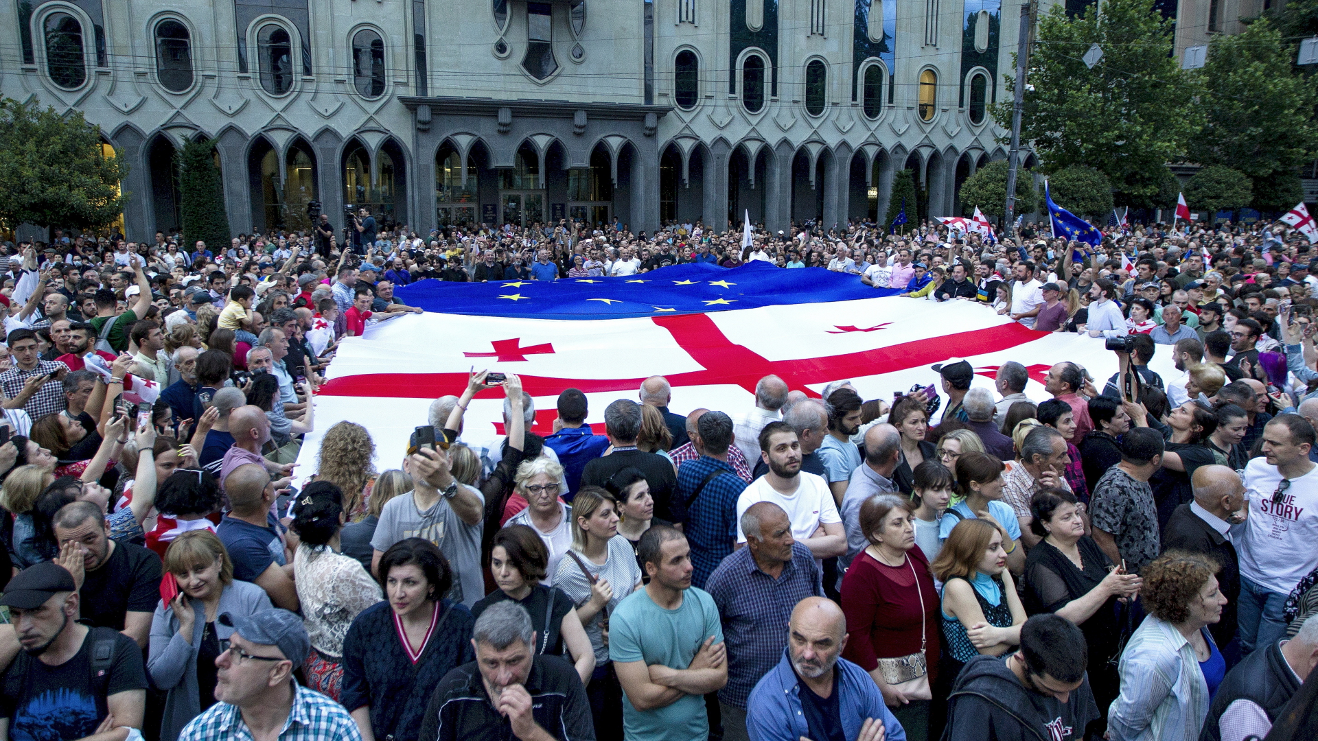 Demonstranten halten eine riesige georgische und eine europäische Fahne während einer Demonstration vor dem Parlamentsgebäude.