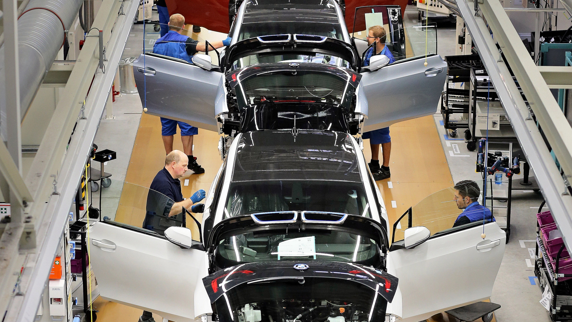 BMW-Mitarbeiter in einer Fertigungshalle an Elektroautos mit offenen Türen, an denen sie arbeiten | dpa