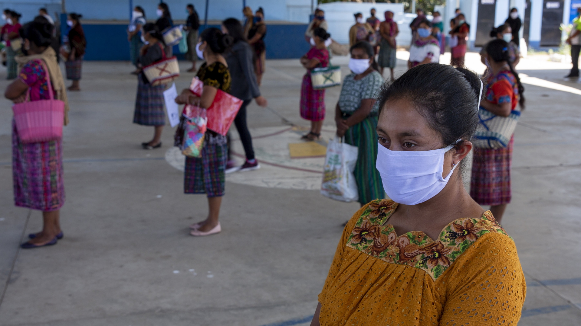 Frau mit Gesichtsmaske steht vor einer Essensausgabe im Dorf Xesuj in Guatemala an  | AP