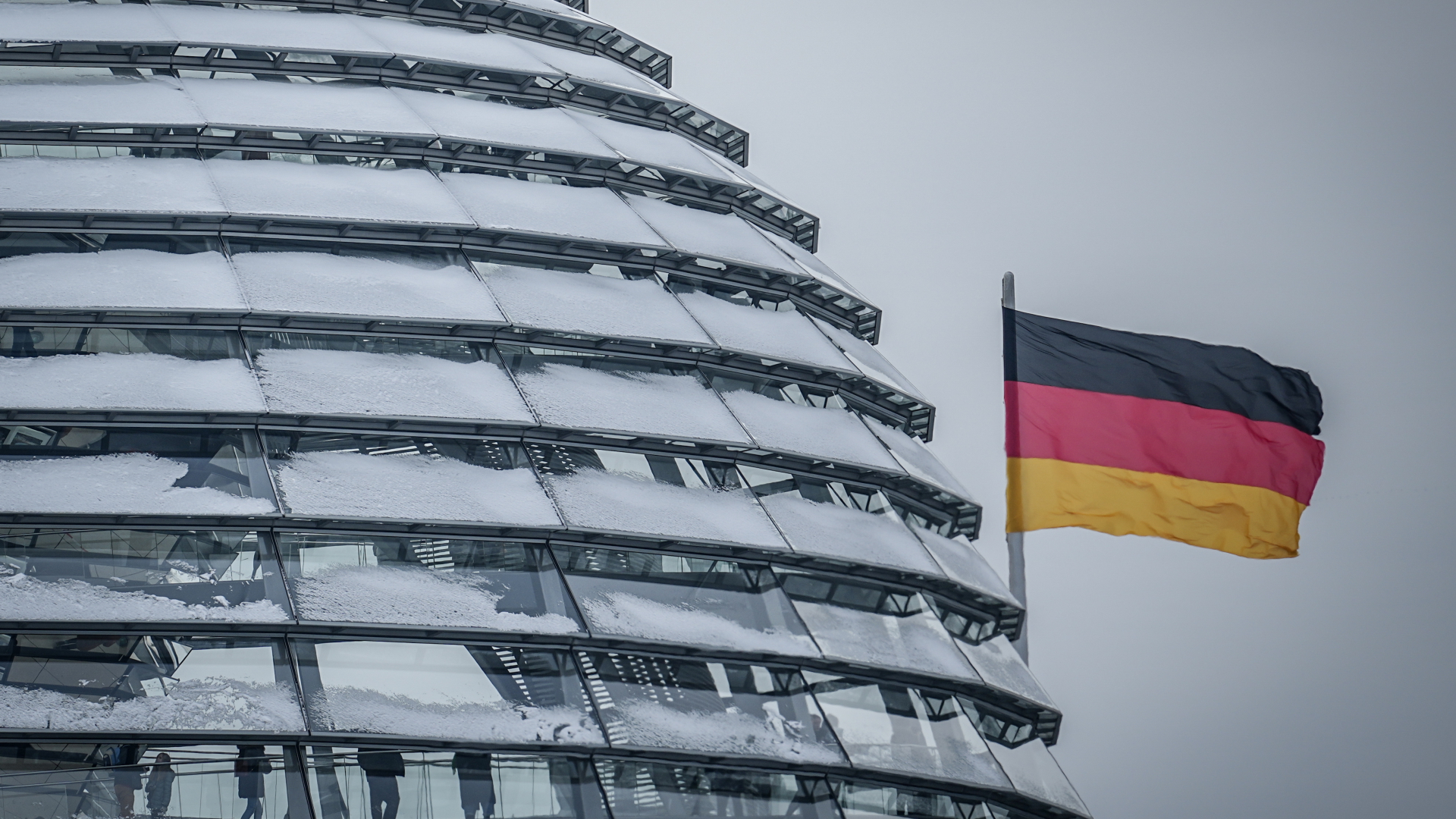 Blick auf die verschneite Kuppel des Reichstagsgebäudes mit einigen Besuchern und deutscher Flagge