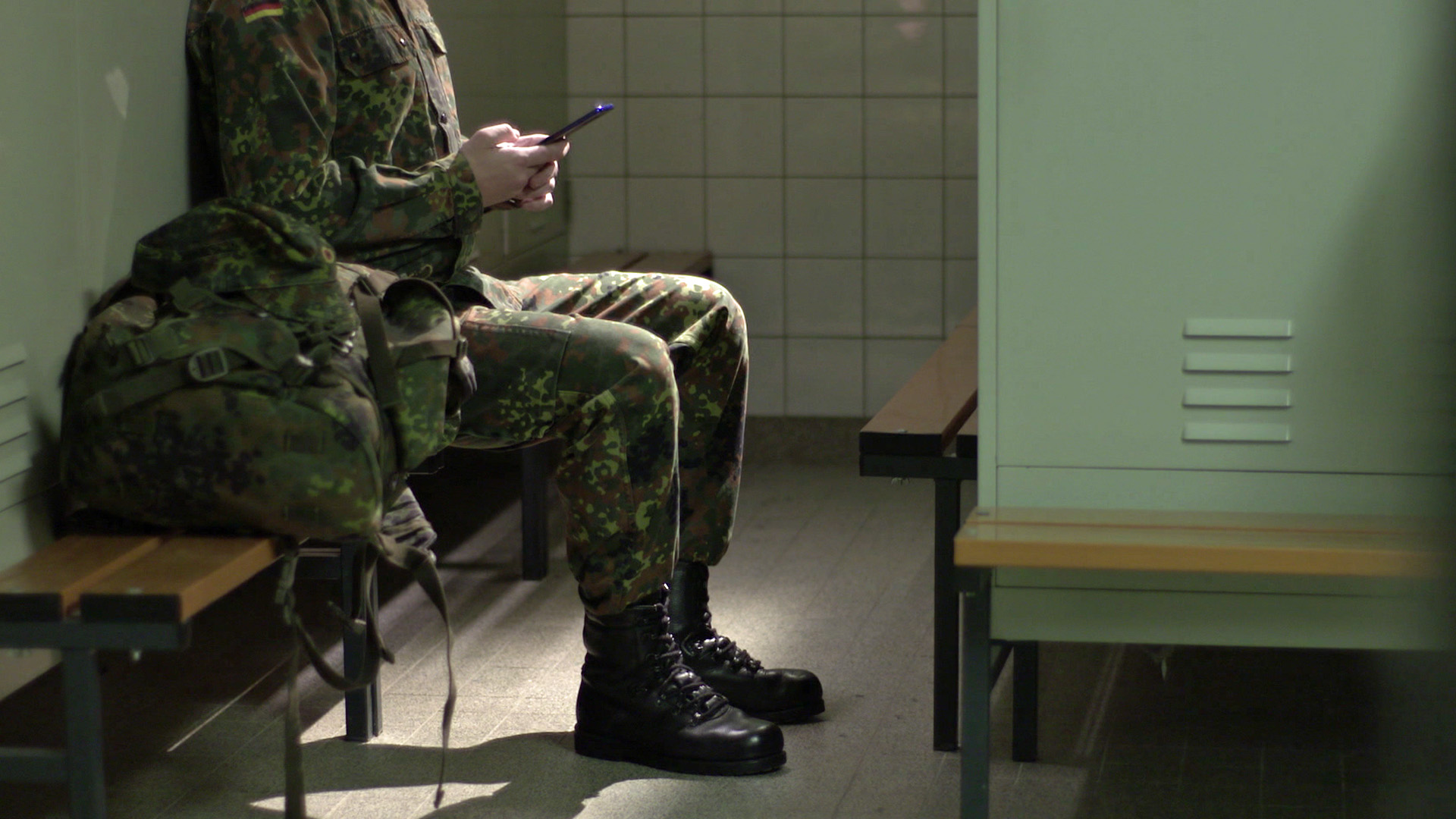Unkenntlich gemachter Soldat sitzt in einer Umkleide mit Smartphone in der Hand. | Honorarfrei