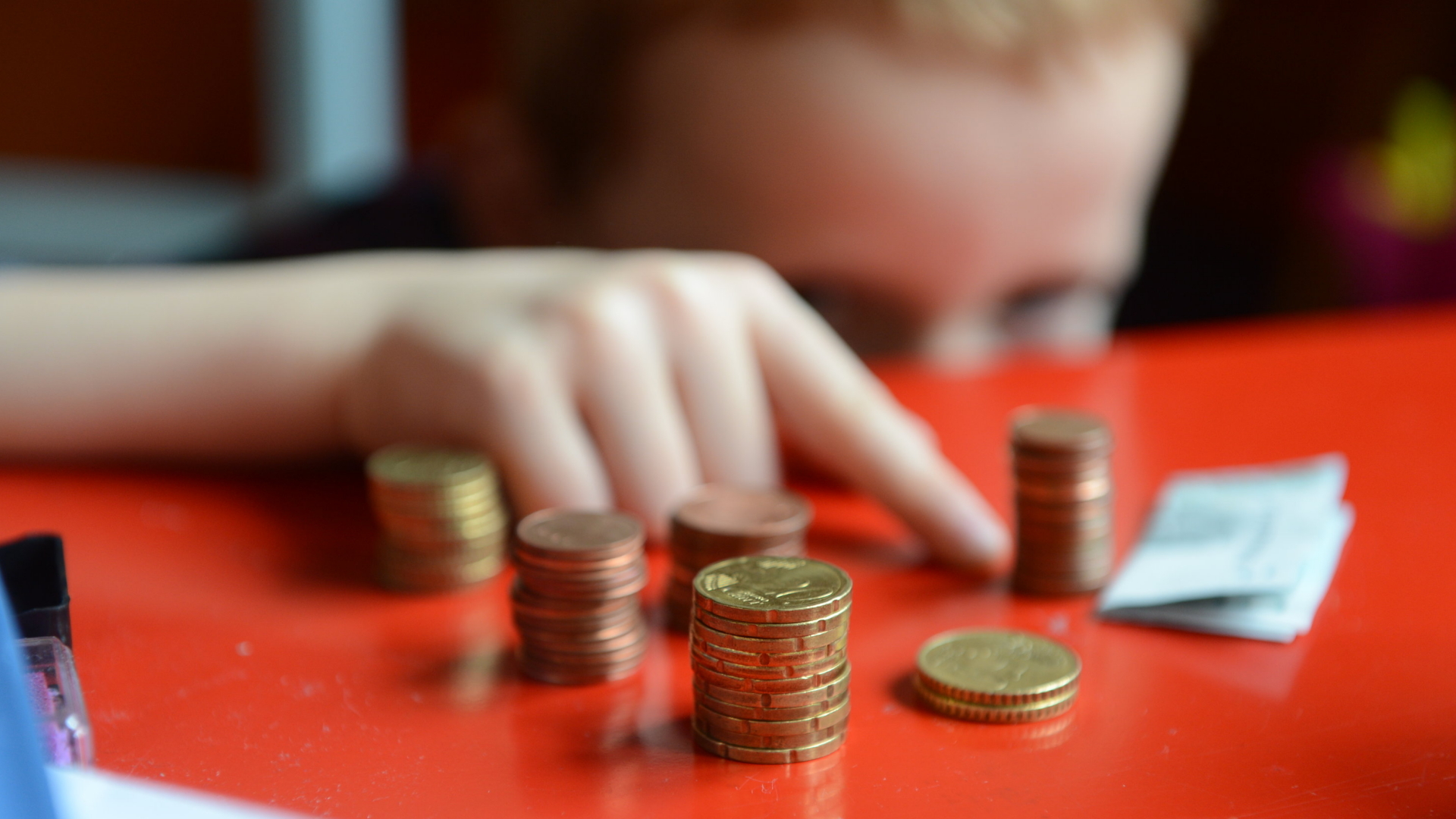 Ein fünfjähriger Junge sitzt an einem roten Tisch und zählt sein gespartes Taschengeld. | dpa