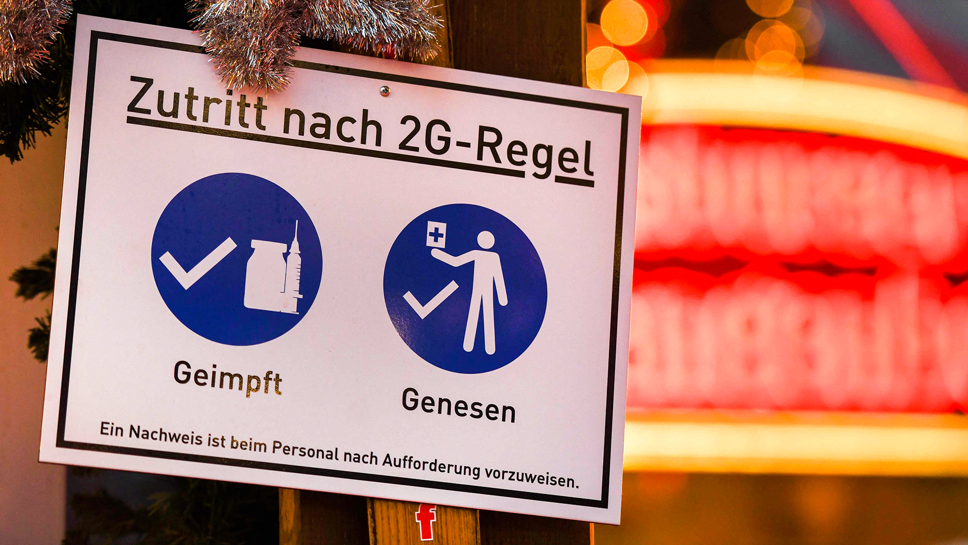 Eine Frau geht auf dem Weihnachtsmarkt in Dortmund an einem Plakat vorbei, das auf die sogenannte 2G-Regel (geimpft oder von Covid-19 genesen) hinweist.