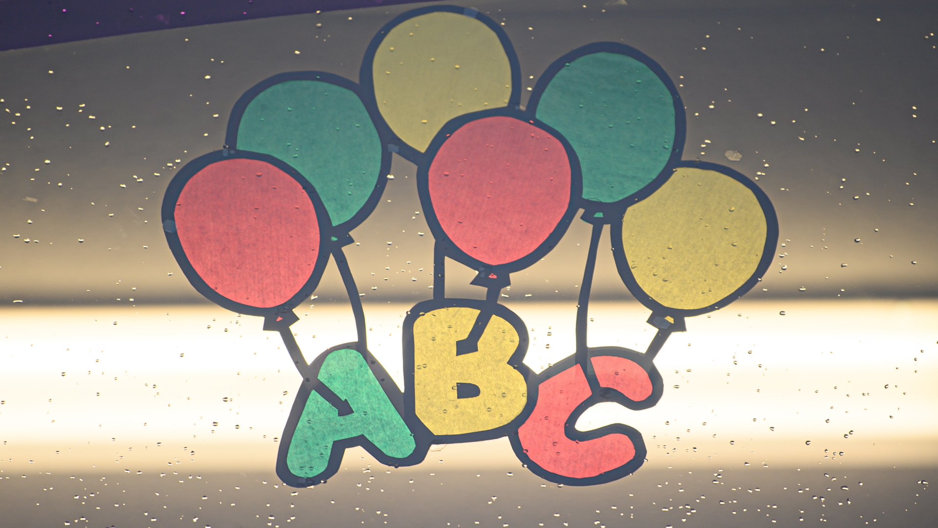 Eine bunte Zeichnung mit den Buchstaben "ABC" und Luftballons klebt an einem Schulfenster. | dpa