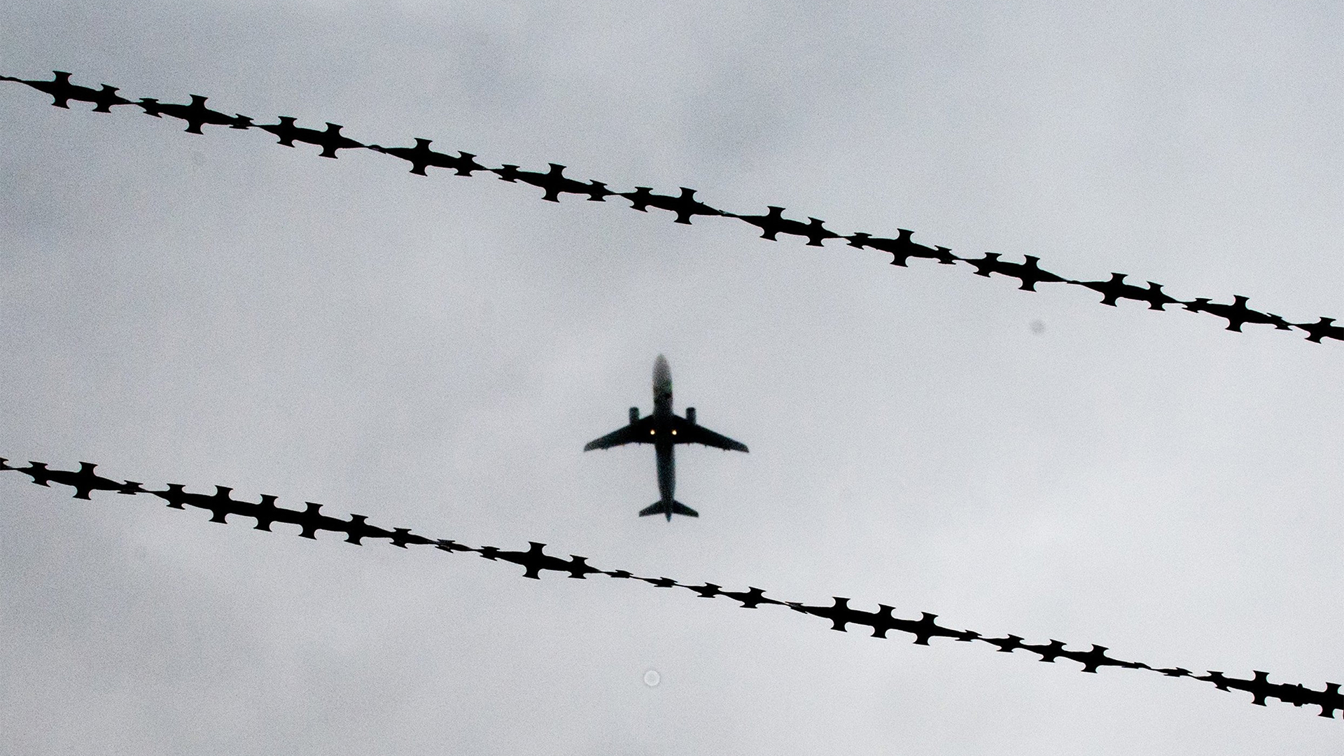 Ein Flugzeug fliegt über einen Stacheldrahtzaun. | Bildquelle: dpa