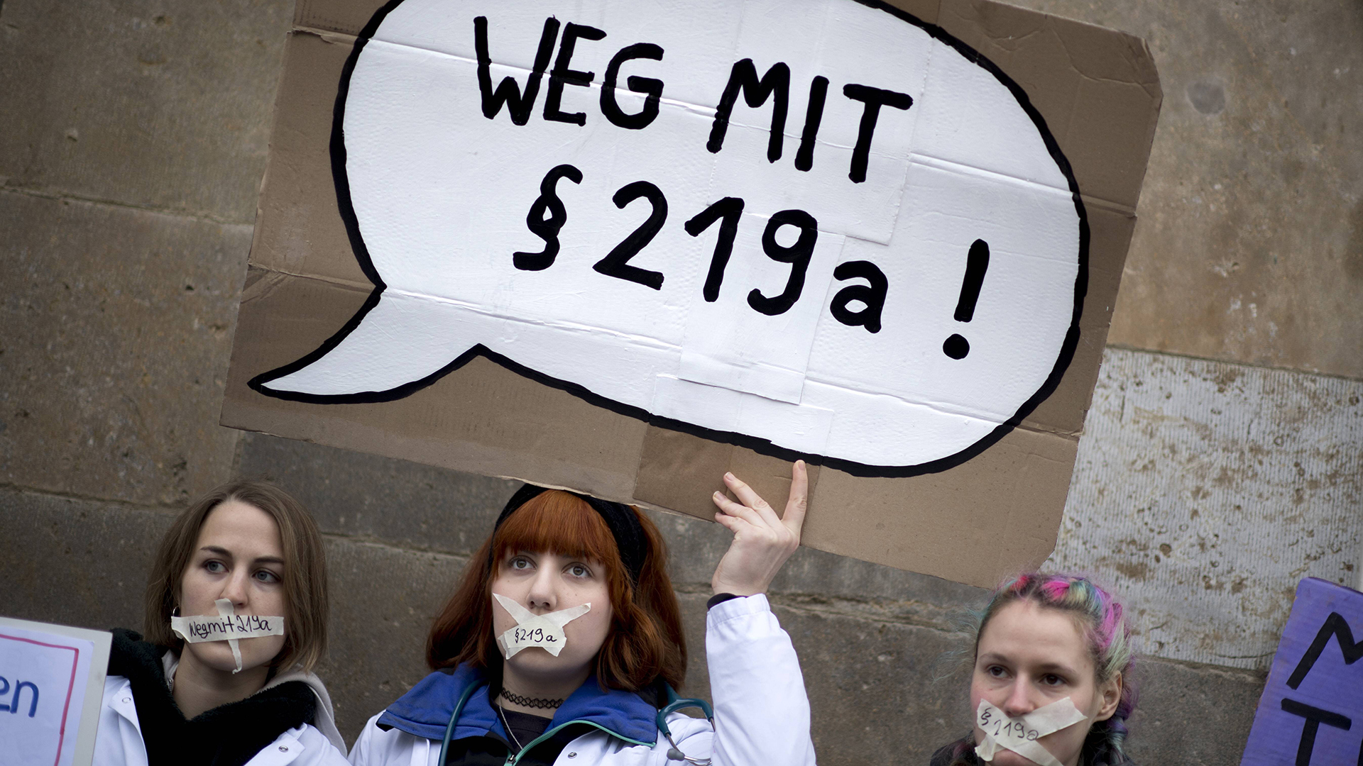 Eine Frau mit einem Plakat "Weg mit 219a" und zugeklebten Mund auf einer Kundgebung. | imago/IPON