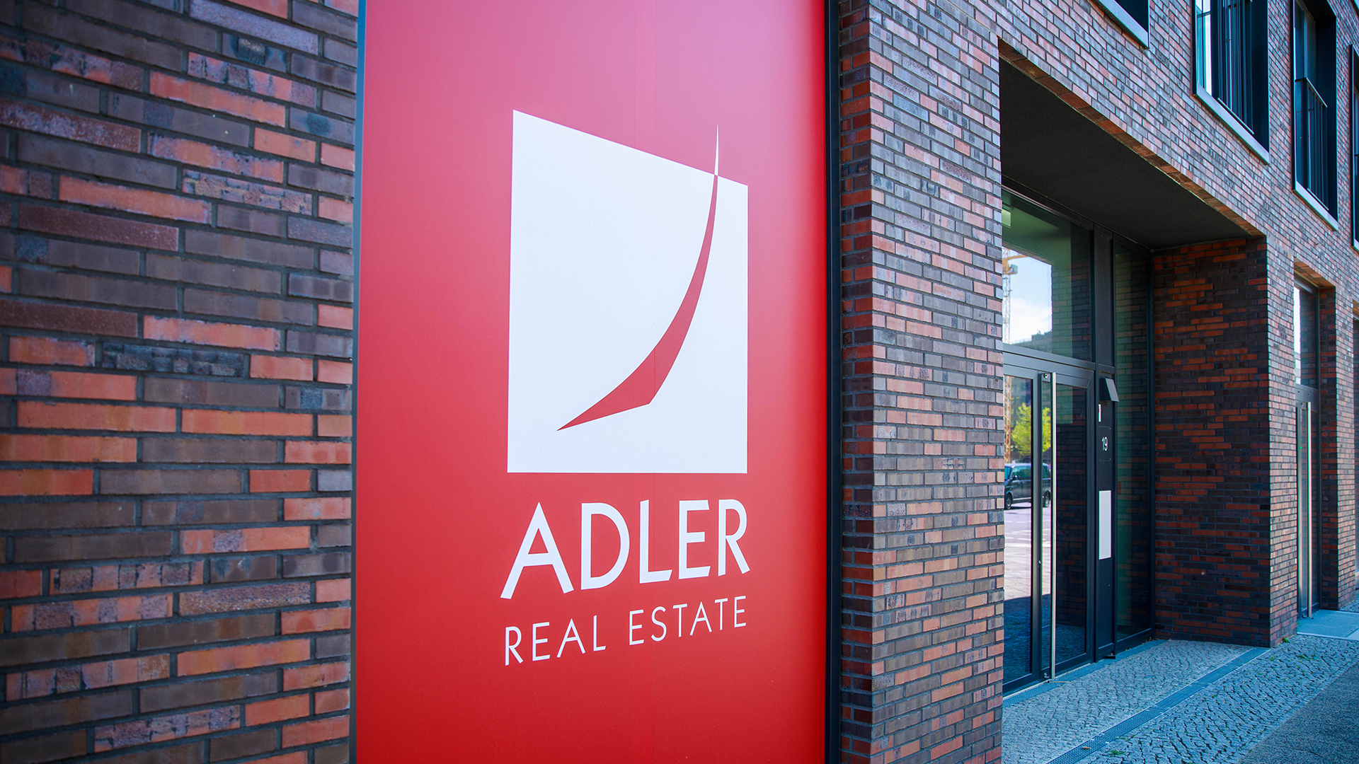 "Adler Real Estate"-Logo an der Front eines Neubaus. 