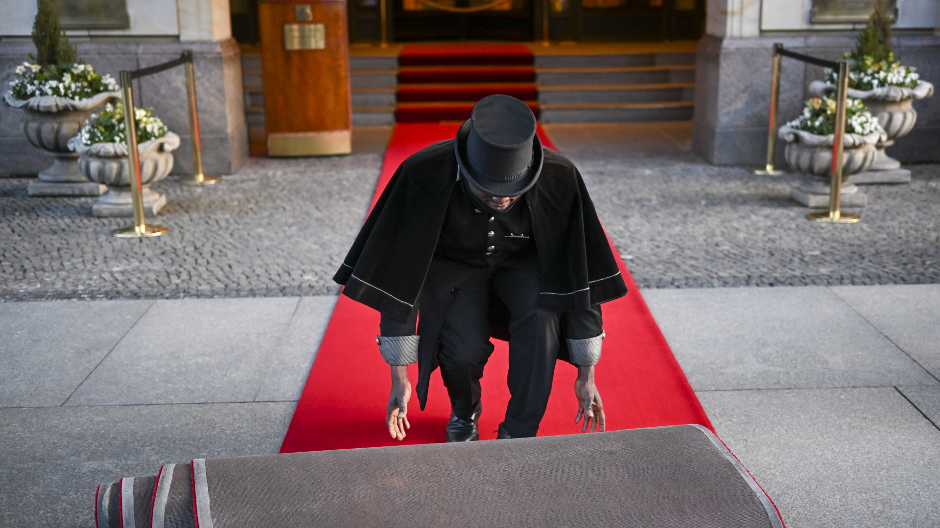 Doorman Timothy Uhunamure rollt vor dem Hotel Adlon in Berlin den roten Teppich aus.