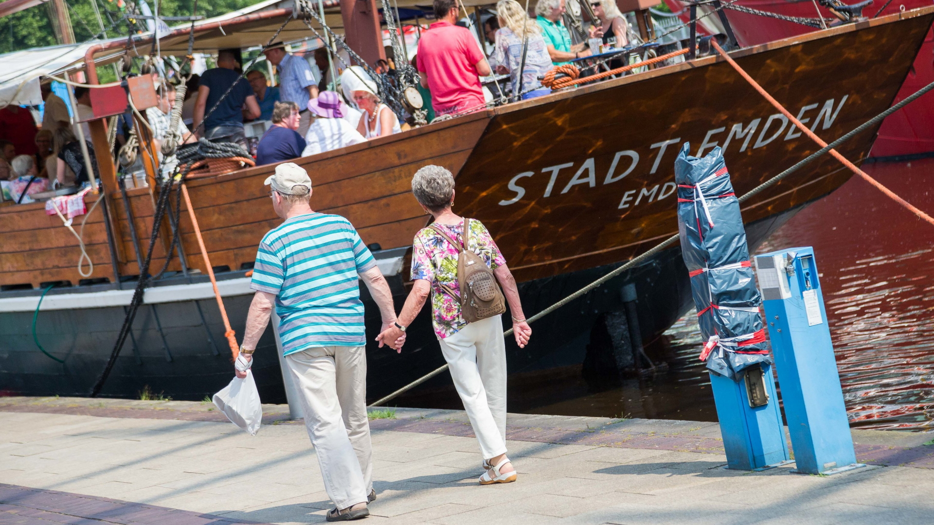 Ein älteres Paar geht Hand in Hand auf ein Schiff zu.