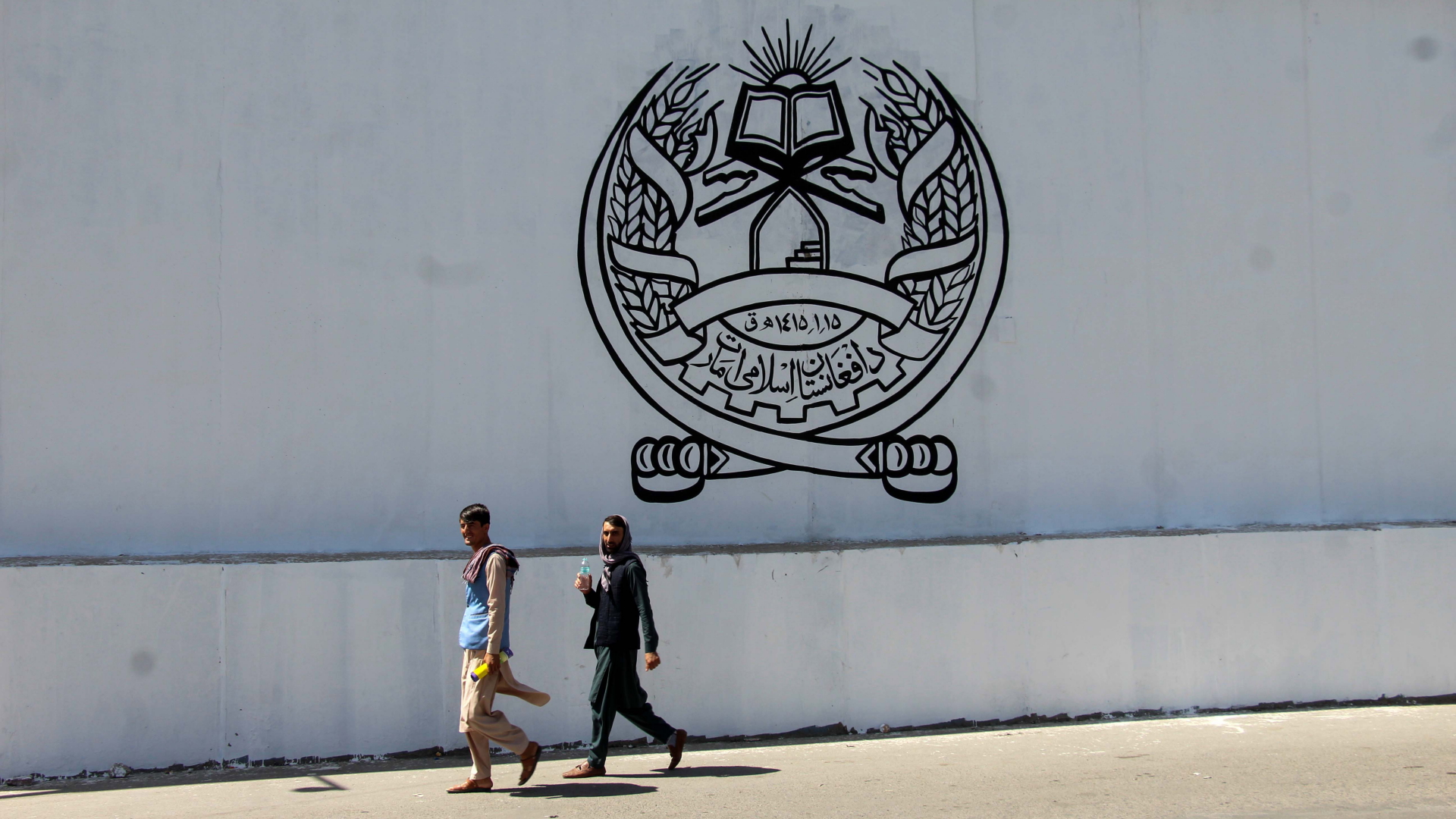 Zwei Männer gehen am Gebäude der ehemaligen US-Botschaft in Kabul vorbei, auf die das Siegel der Taliban gesprüht ist. | EPA