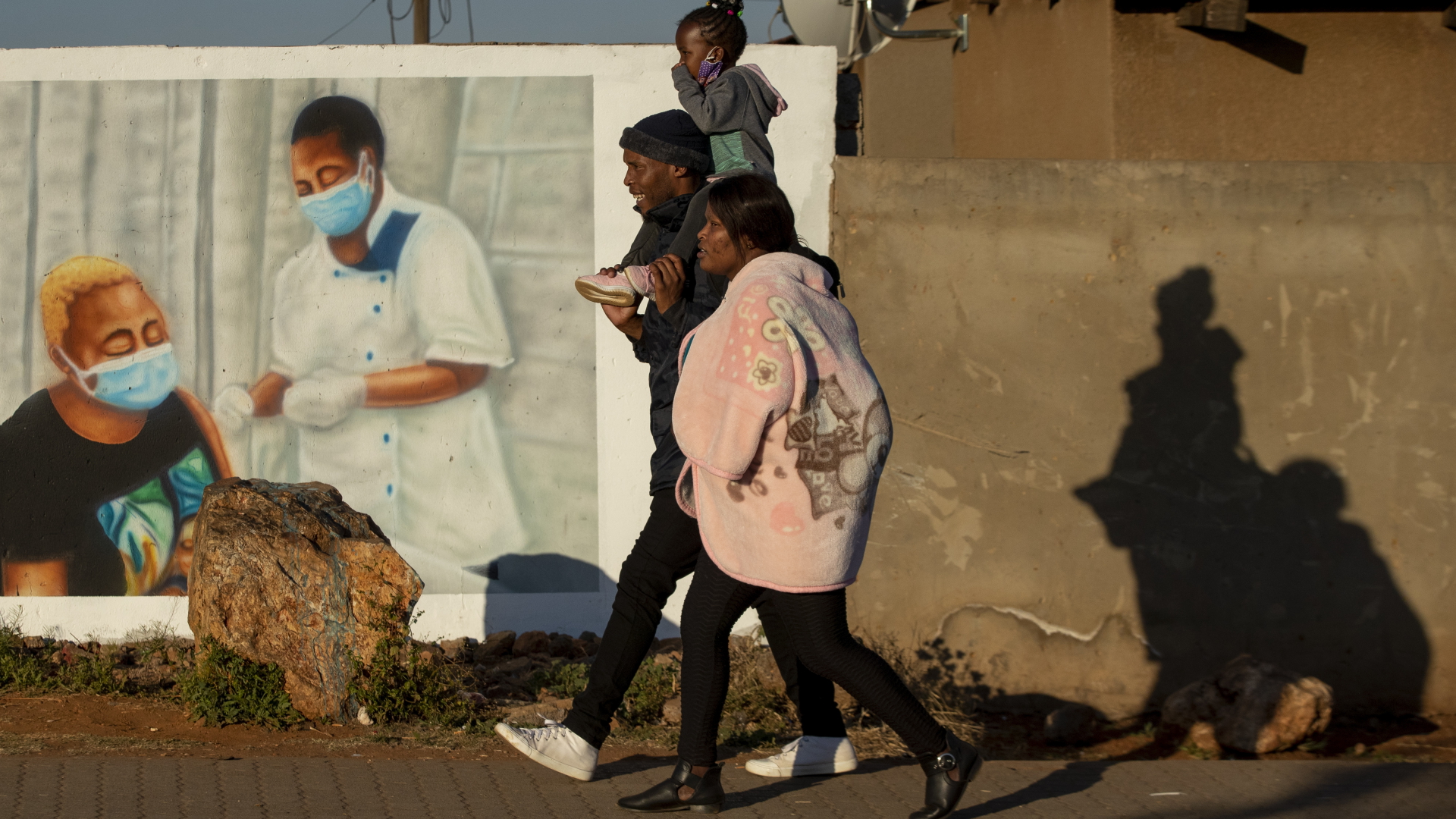 Eine Familie geht an einem Wandbild vorbei, das für die Impfung wirbt | dpa