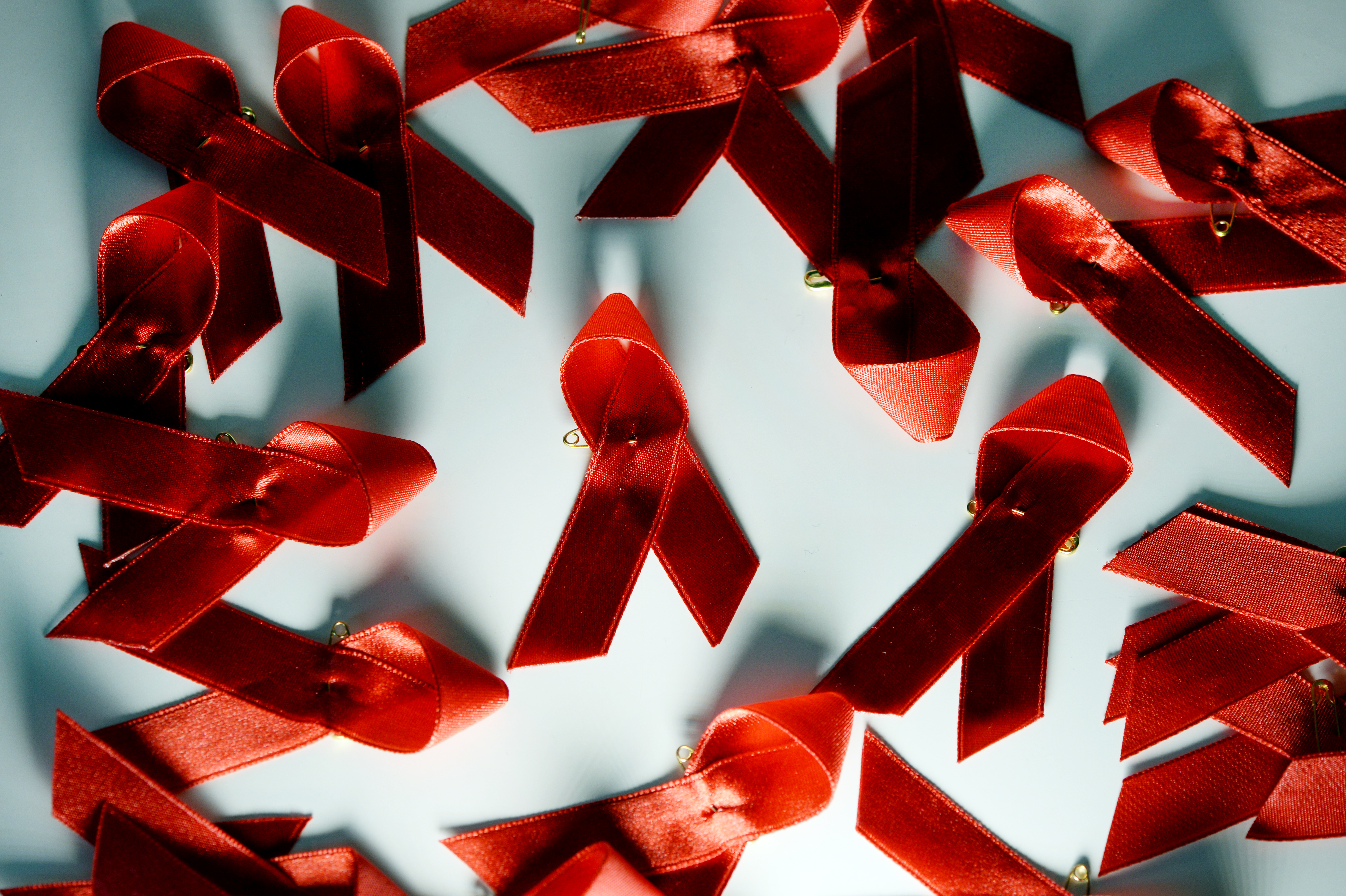 Rote Aids-Schleifen liegen auf einem Tisch.  | dpa