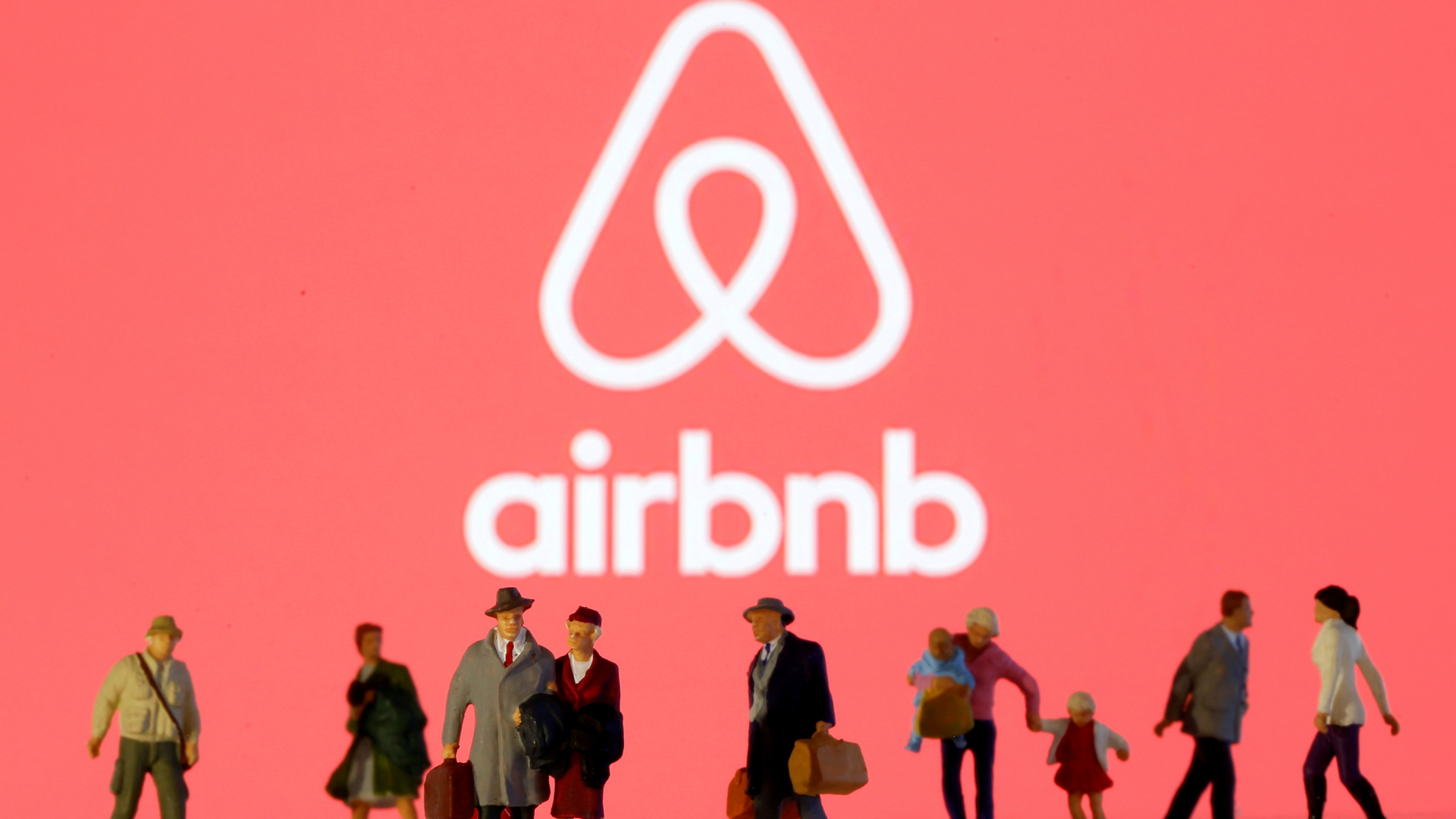 Menschen sind als Spielfiguren aufgereiht, im Hintergrund der Schriftzug des Airbnb-Logos. | REUTERS