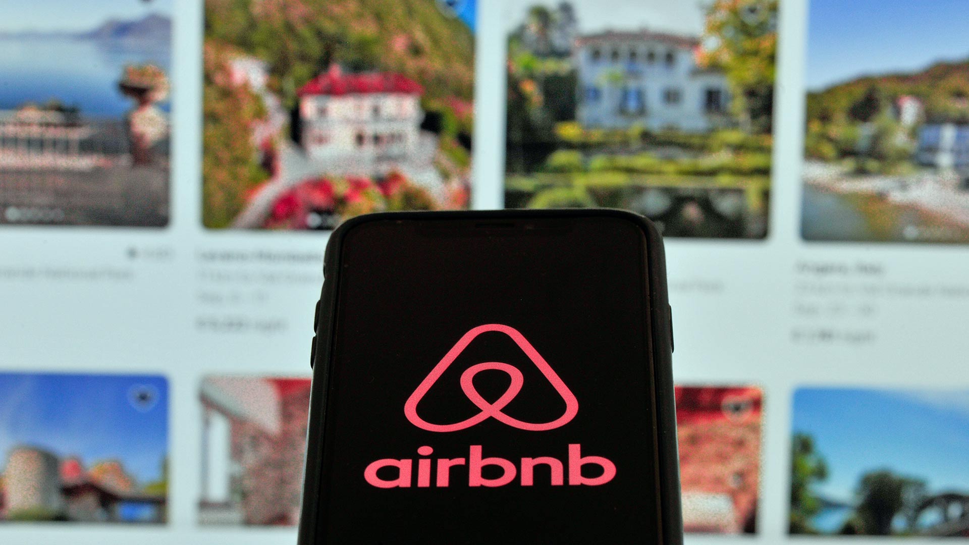 Airbnb-Logo auf einem Smartphone und im Hintergund eine Website mit Mietimmobilien.