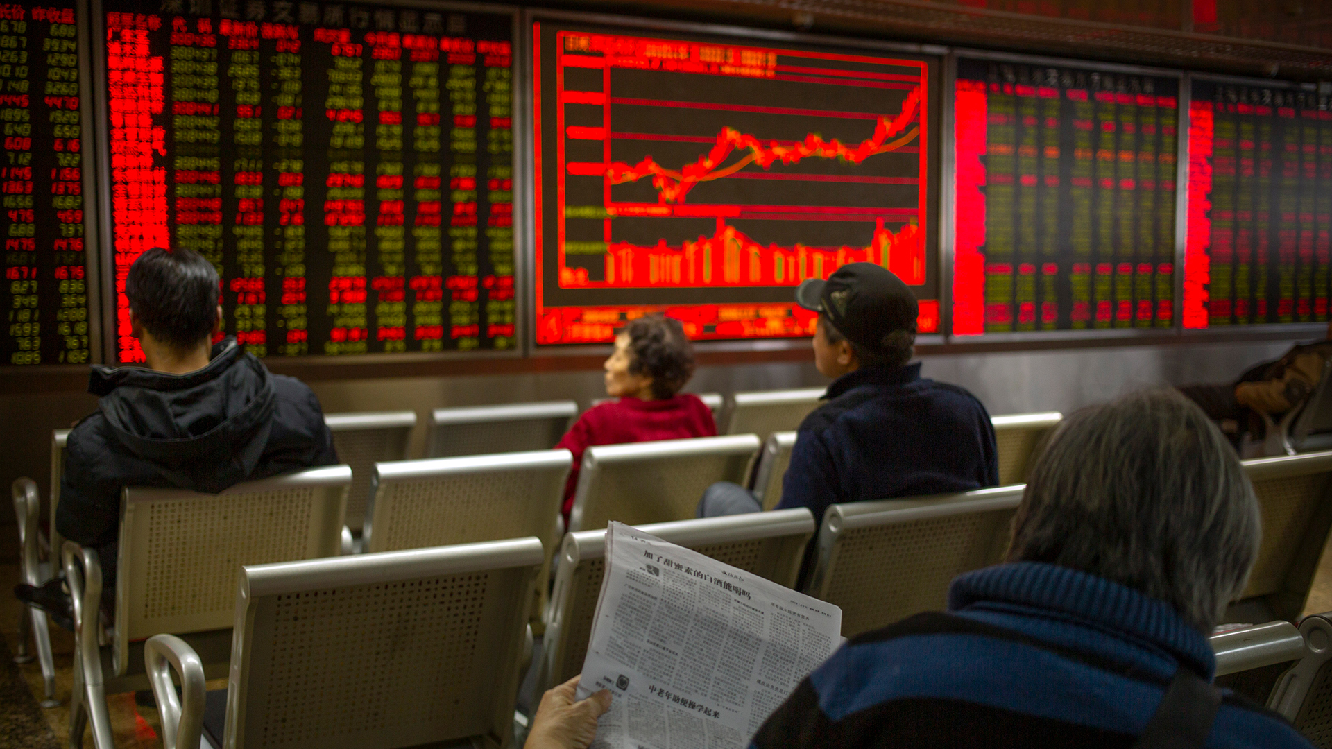 Ein chinesischer Investor liest eine Zeitung, während er die Aktienkurse in einem Brokerhaus beobachtet. | picture alliance/dpa/AP