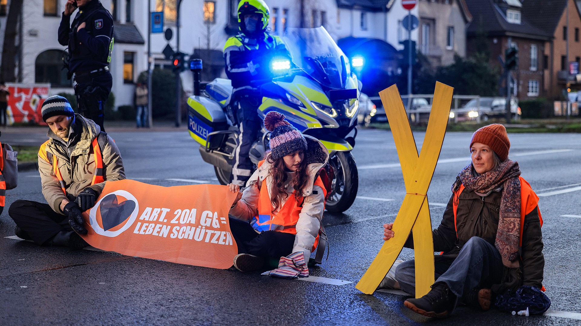 Aktivisten blockieren eine Straße und zeigen ein großes ein gelbes Kreuz | dpa