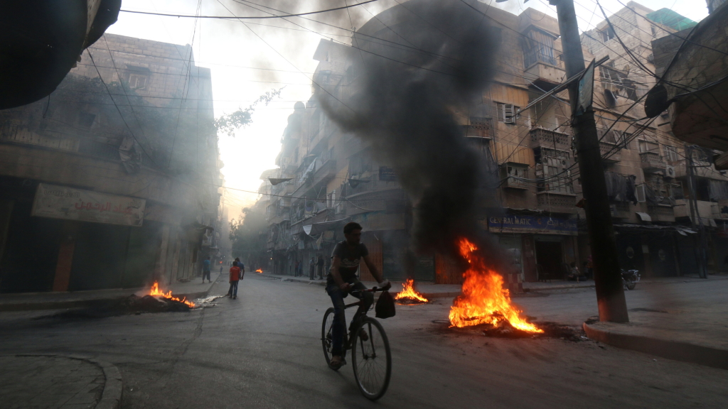 Ein Mann fährt Fahrrad auf brennender Straße von Aleppo