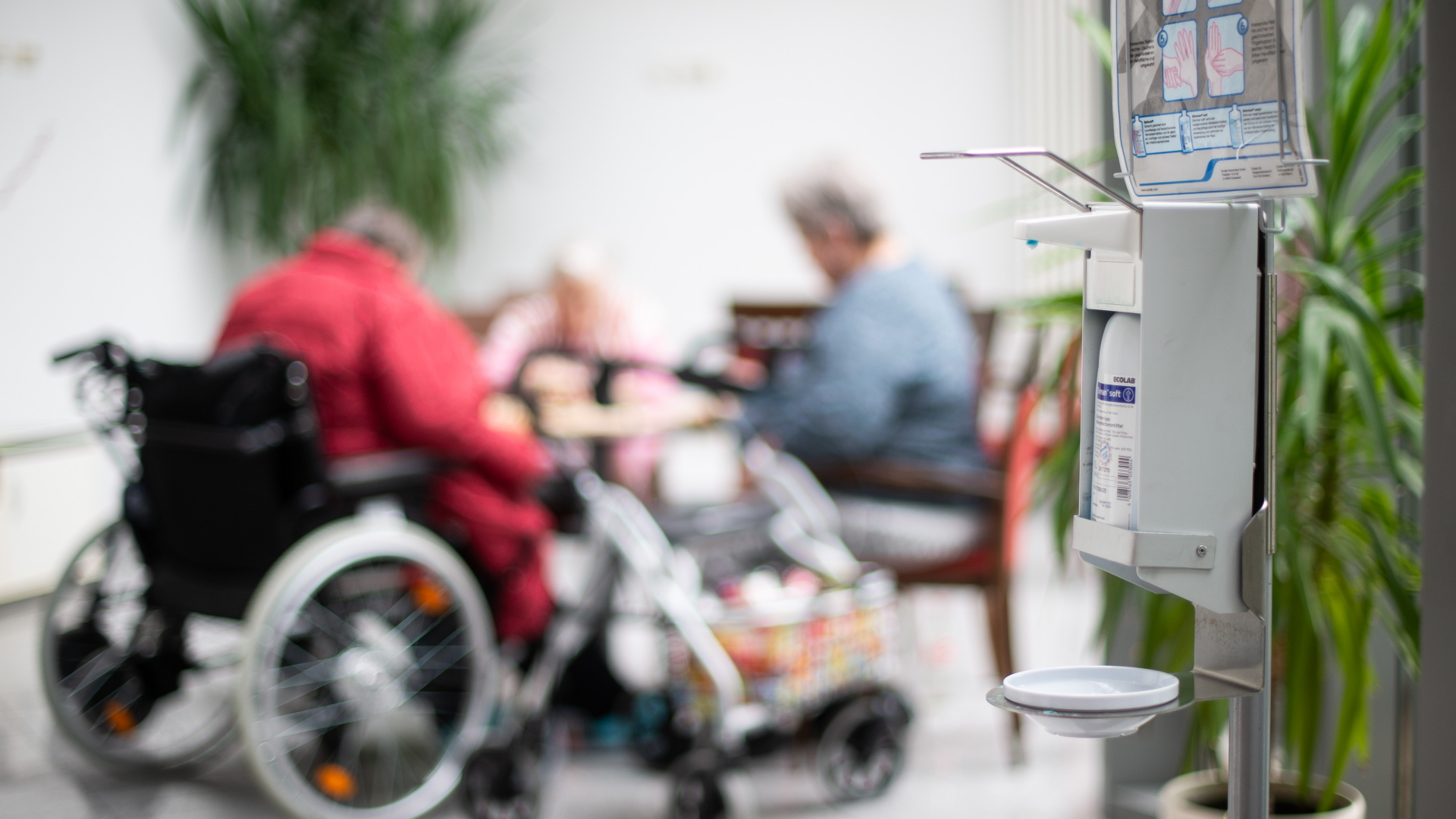 Nordrhein-Westfalen, Heinsberg: Ein Desinfektionsmittelspender hängt im Johannes-Sondermann-Haus des AWO Altenzentrums während im Hintergrund Seniorinnen spielen. | dpa