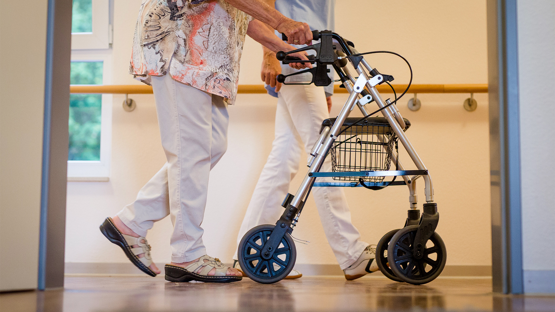 Eine Pflegekraft geht in einem Pflegeheim mit einer älteren Dame über einen Korridor. | dpa