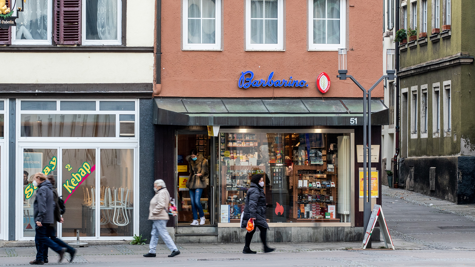 Menschen mit Mundschutz laufen in Cannstatt-Mitte an einem Kiosk und Kebabladen vorbei. | picture alliance / Eibner-Presse