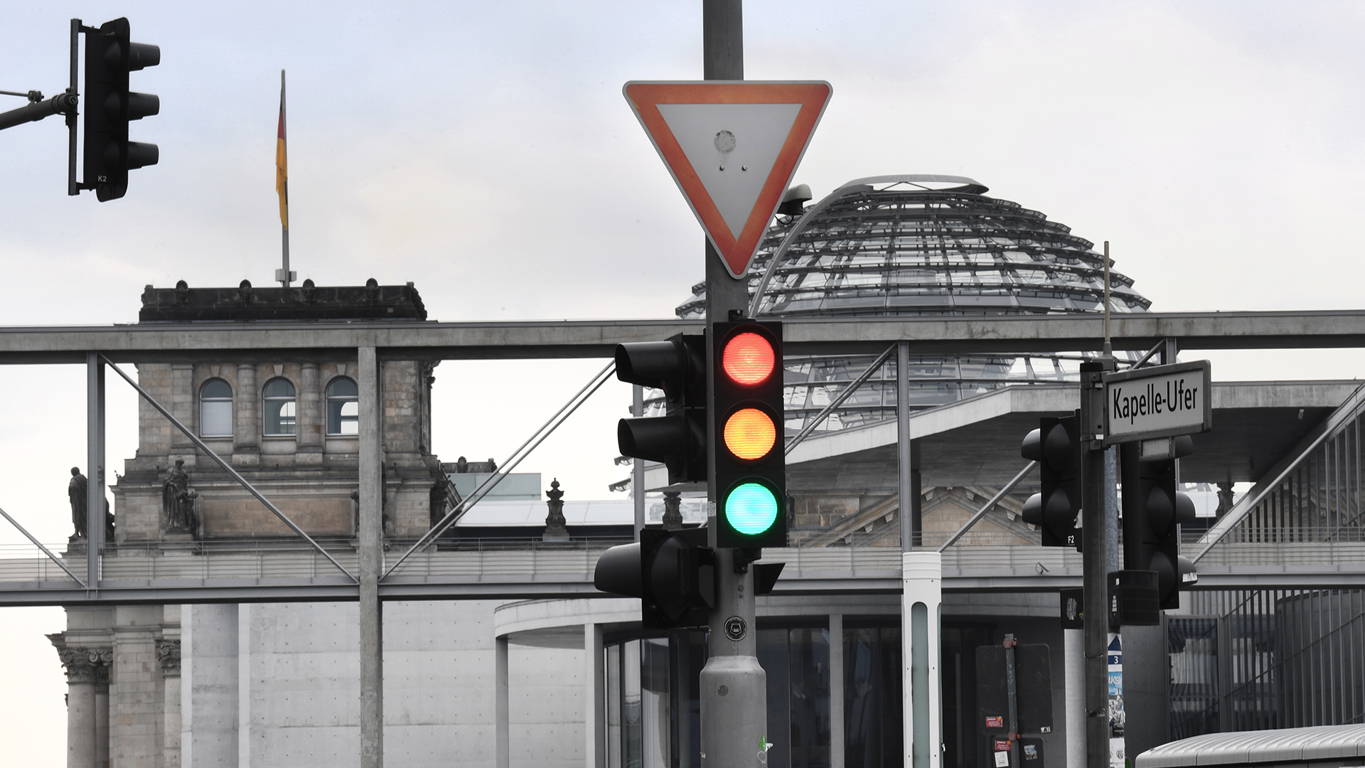 Eine Ampel, an der für einen Moment die Farben Rot, Gelb und Grün gleichzeitig leuchten, ist im Regierungsviertel vor der Kuppel des Reichstagsgebäudes zu sehen. | dpa