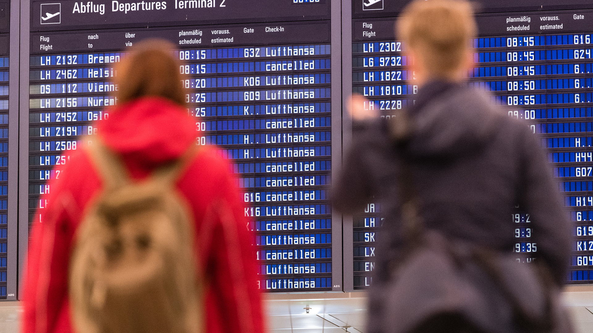 Zwei Passagiere stehen vor einer Anzeigetafel am Flughafen in München | dpa