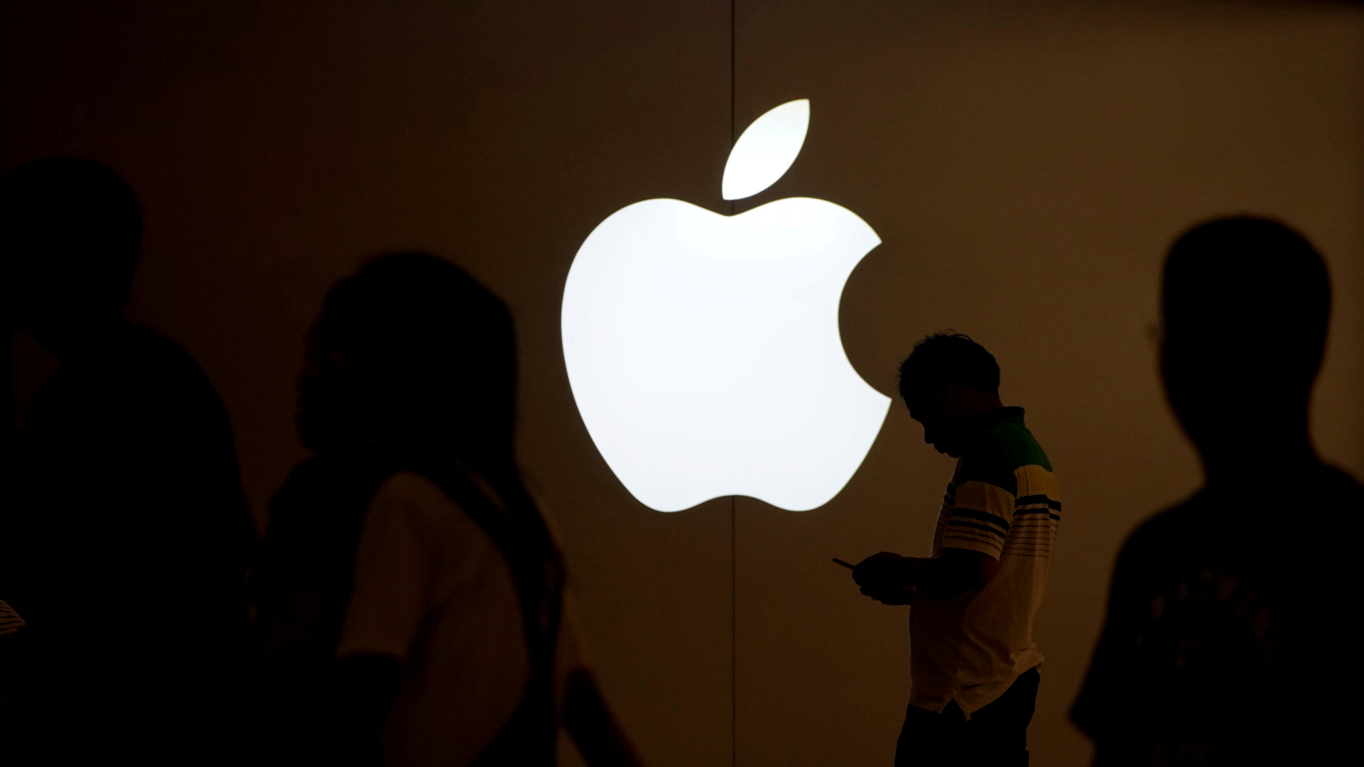 Ein Mann schaut vor dem Logo von Apple auf das Display seines Handys. | Bildquelle: REUTERS