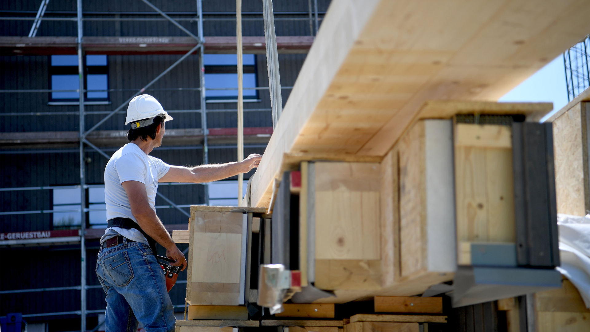 Ein Arbeiter hängt einen Holzbalken an einen Kran auf einer Baustelle der Wohnungsbaugesellschaft Howoge. 