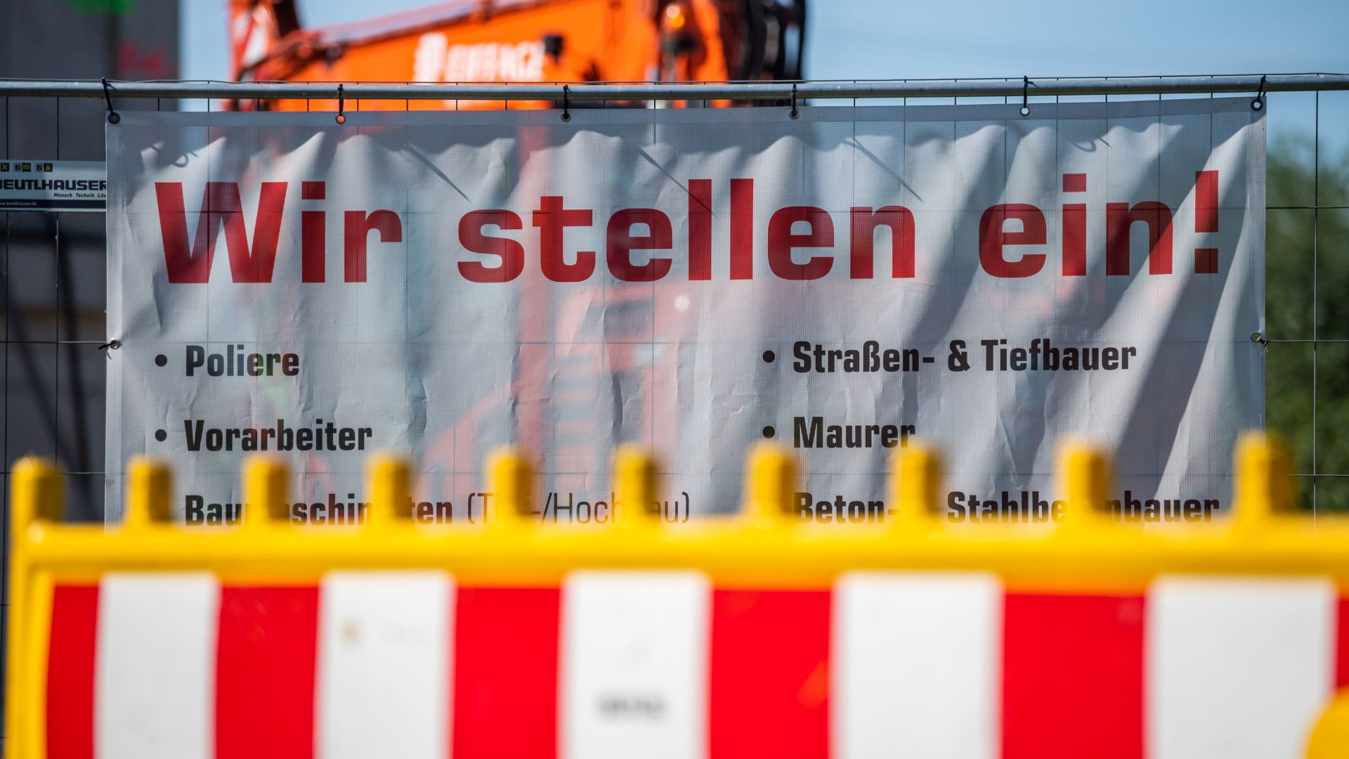 An einem Bauzaun einer Baustelle hängt ein Banner mit der Aufschrift "Wir stellen ein!" (Archivbild vom 03.06.2020) | dpa