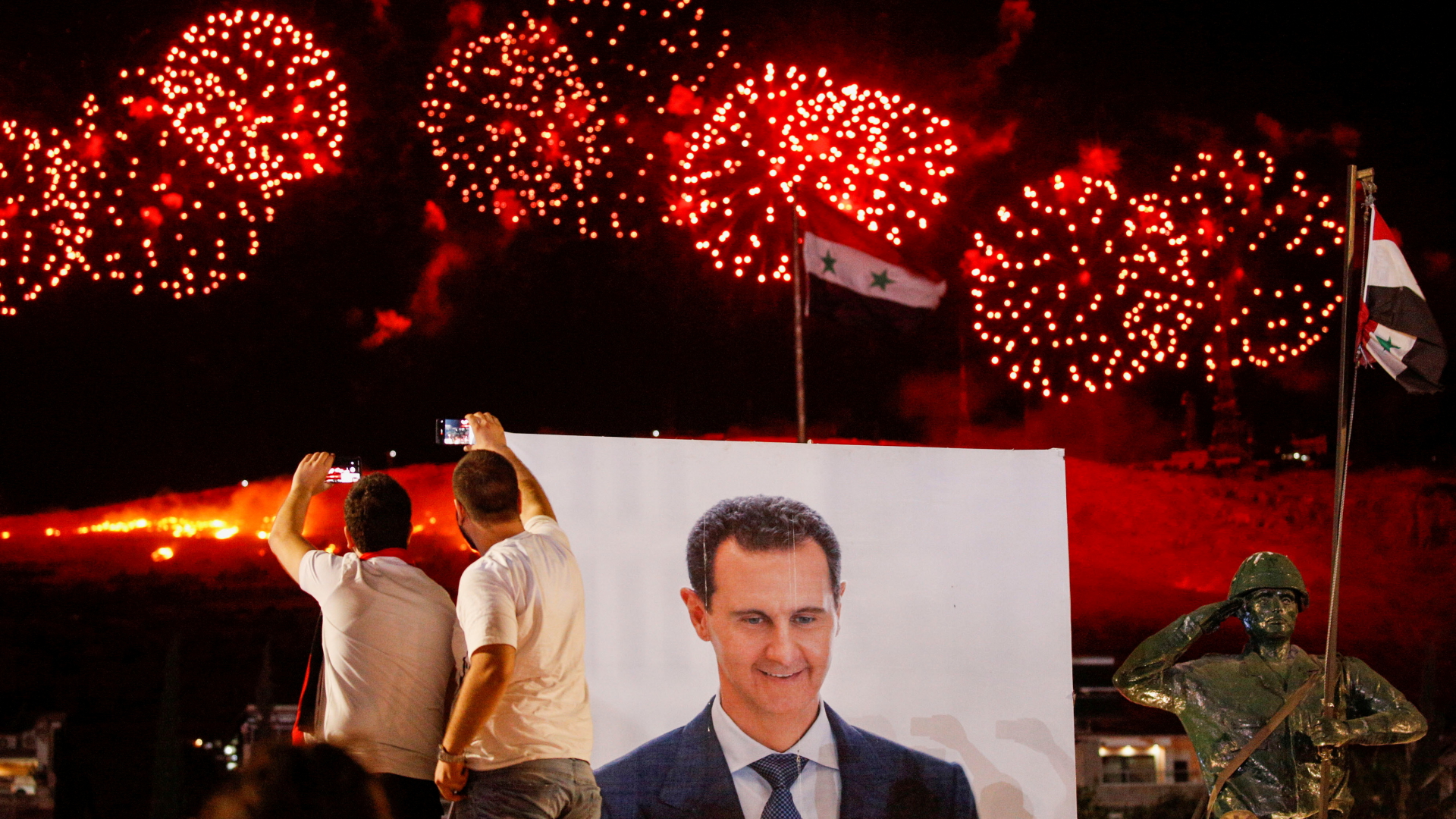 Anhänger des syrischen Präsidenten Assad schauen sich ein Feuerwerk vor einem Plakat mit Assads Konterfei an. | REUTERS