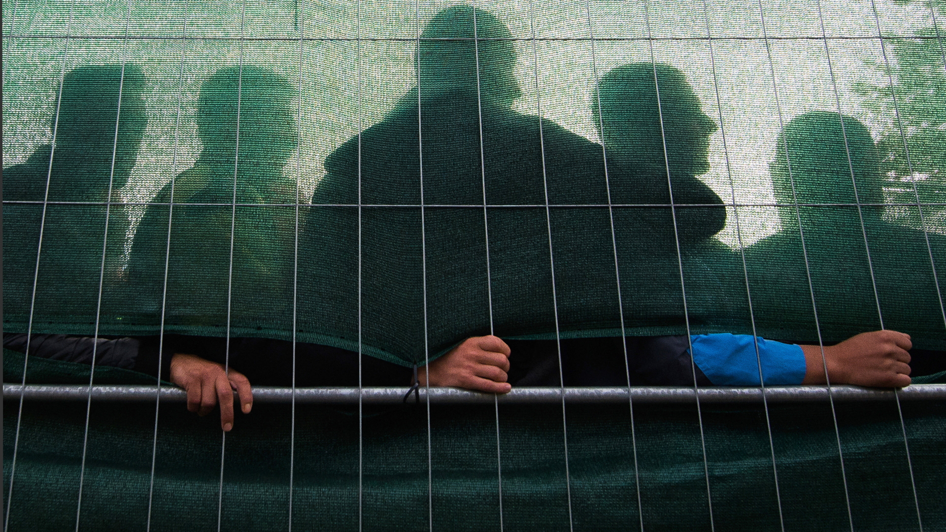 Flüchtlinge stehen hinter einer mit Plane verhangenen Absperrung.