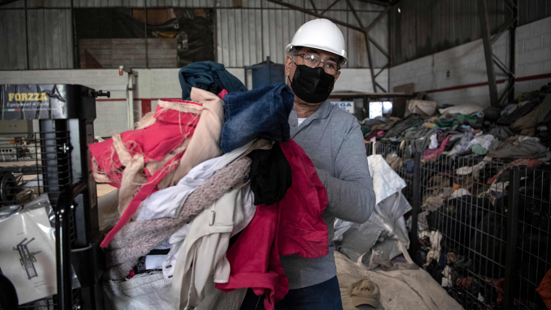 Ein Mann trägt alte Kleidung in einer Recycling-Fabrik in Chile. | AFP