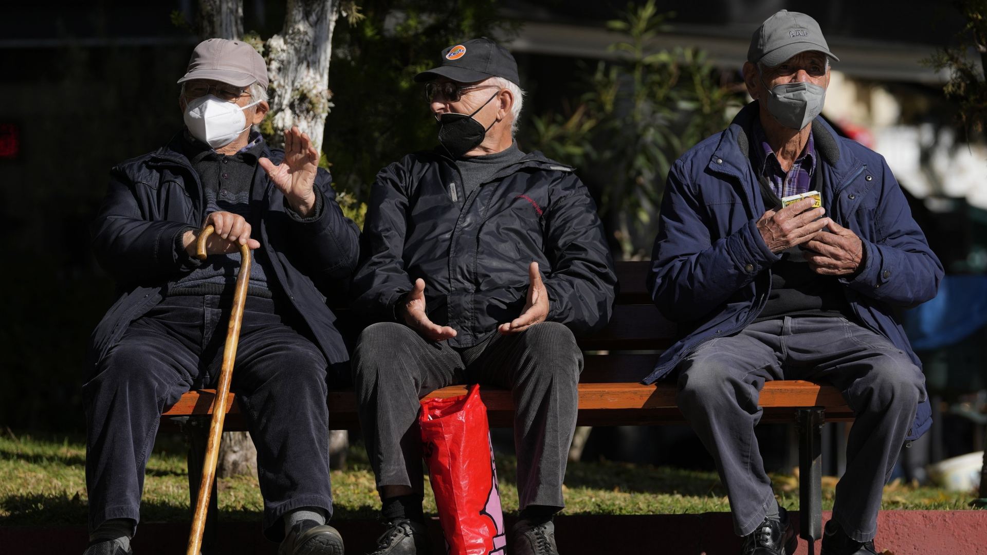 Drei ältere Männer mit FFP2-Masken sitzen auf einer Bank in Athen, Griechenland. | AP