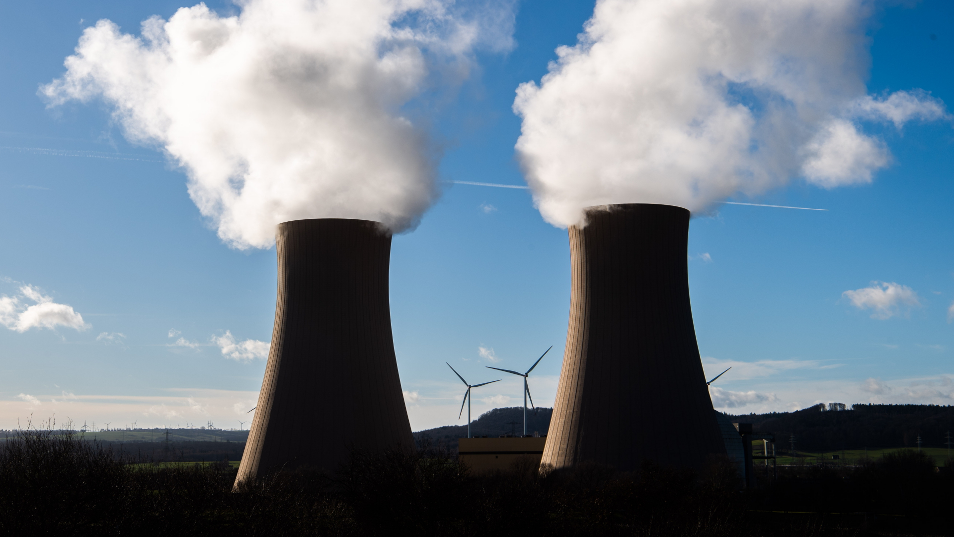 Dampf steigt aus den Kühltürmen des Atomkraftwerks Grohnde im Landkreis Hameln-Pyrmont auf, während im Hintergrund Windräder zu sehen sind | dpa