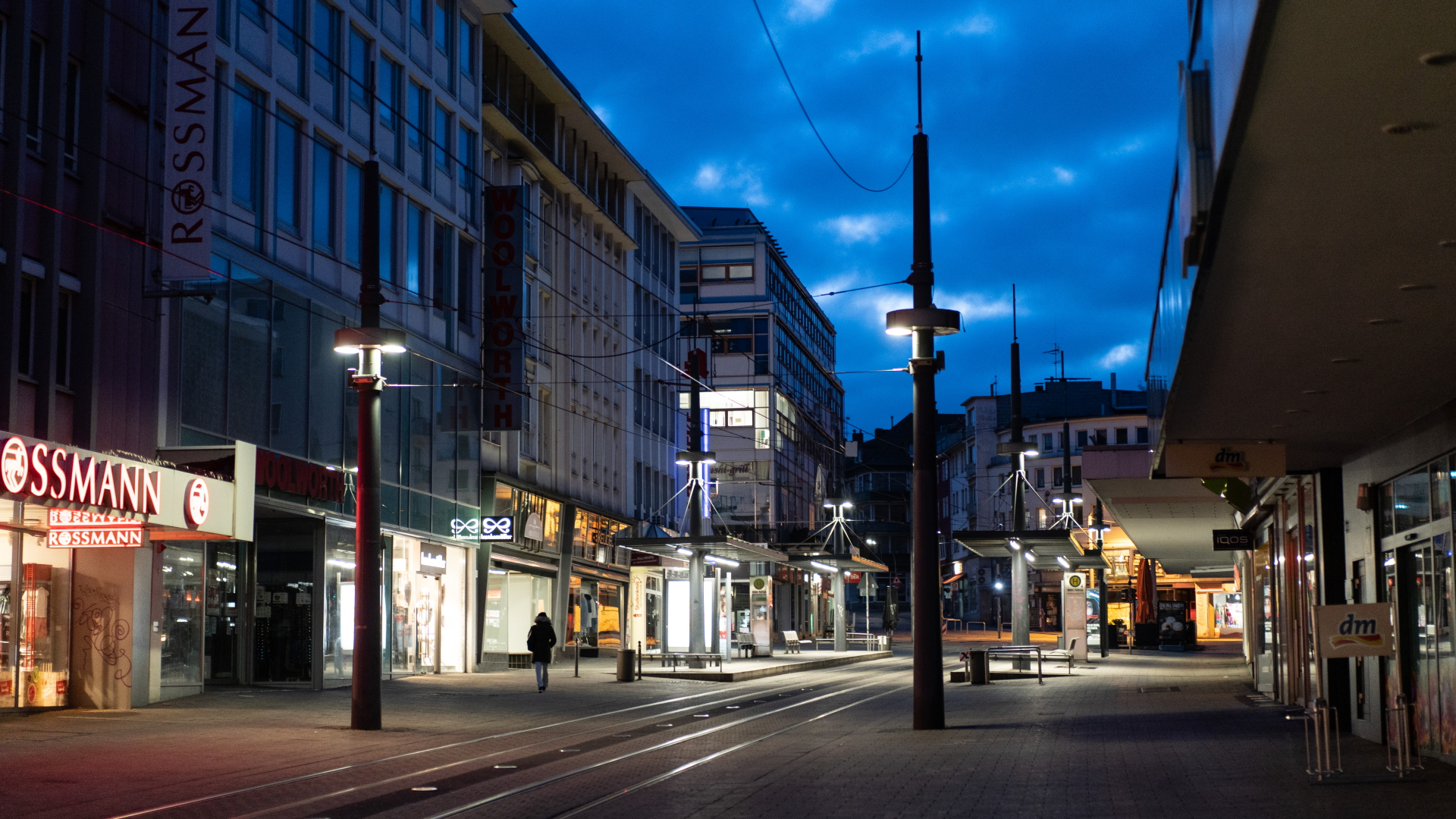 Ein Mann geht in der sogenannten blauen Stunde an den Geschäften in der ansonsten leeren Fußgängerzone vorbei. | dpa
