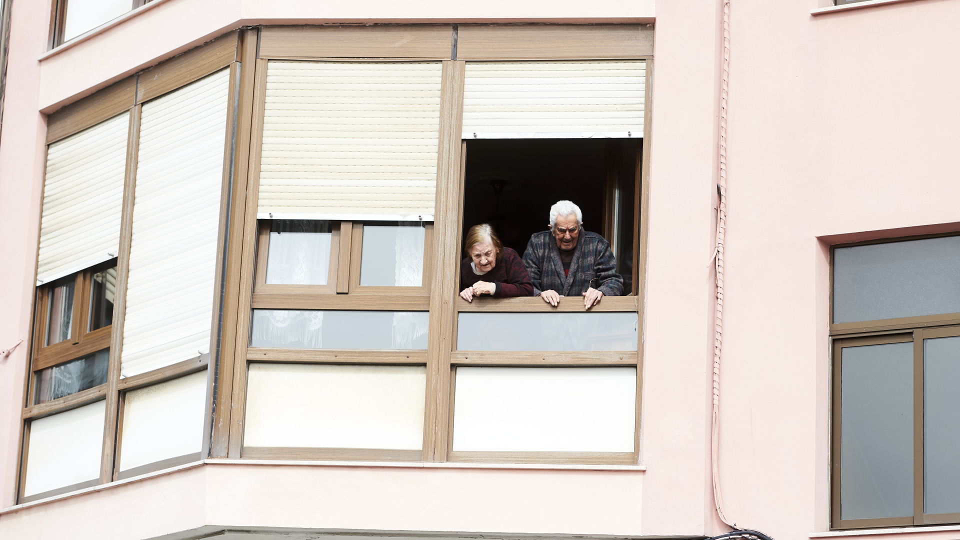Ein älteres Paar steht am offenen Wohnungsfenster. | dpa