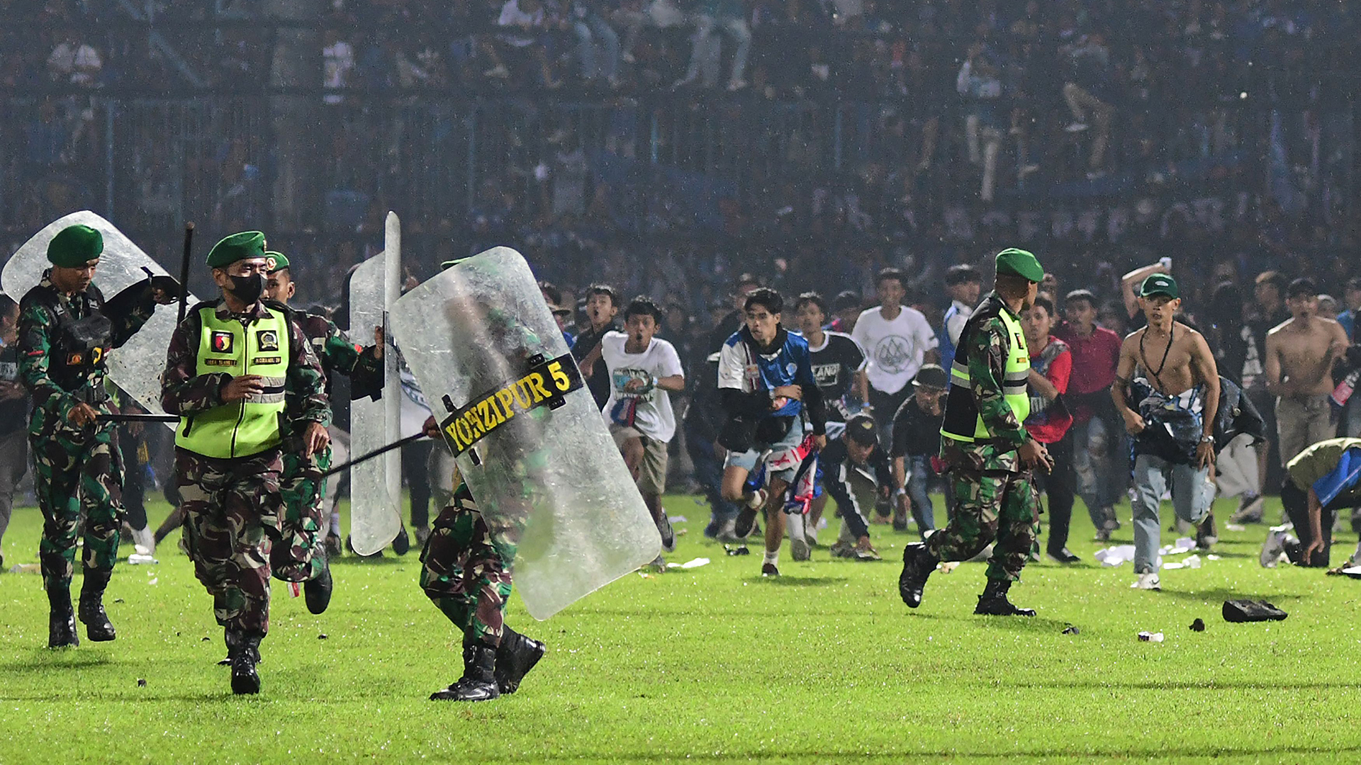 Fans des Arema FC, die nach einem Fußballspiel zwischen dem Arema FC und Persebaya im Stadion Kanjuruhan auf dem Spielfeld auf Mitglieder der indonesischen Armee zulaufen. | AFP