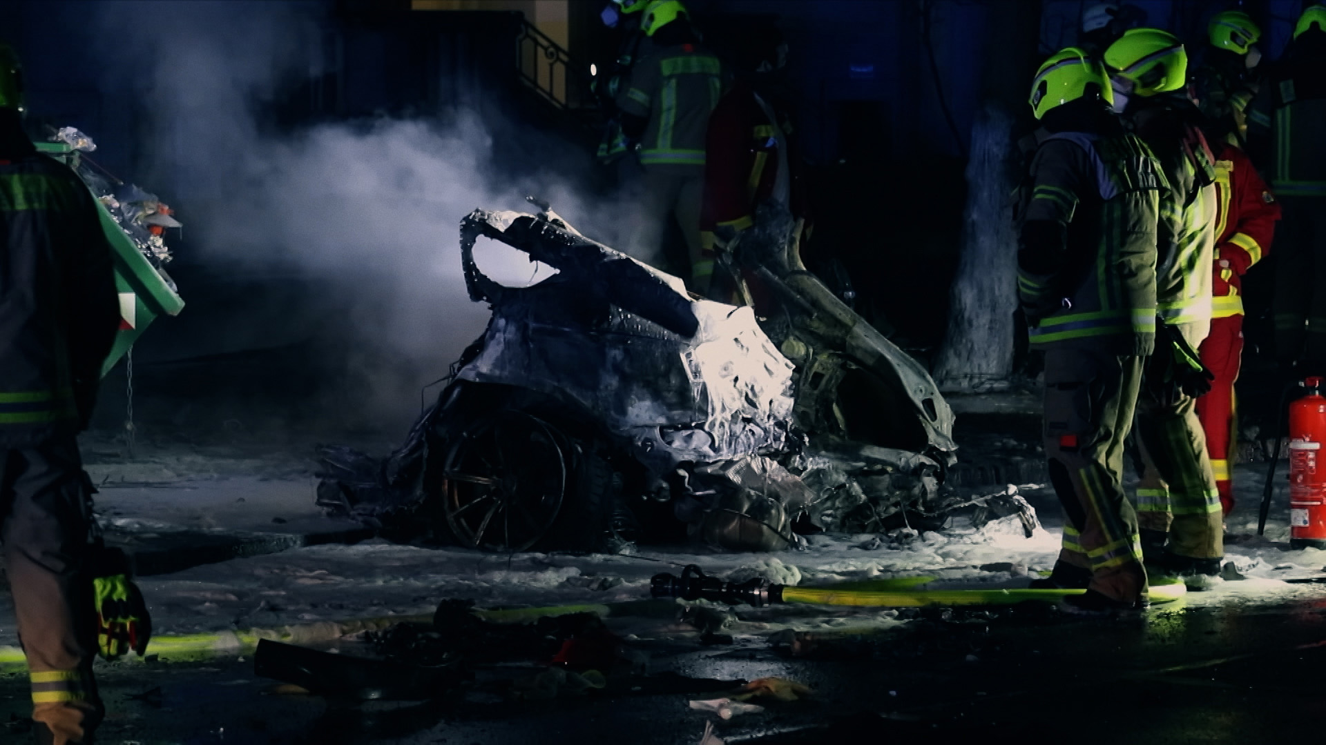 Feuerwehrleute stehen vor einem ausgebrannten Unfallauto. | Frank Talke