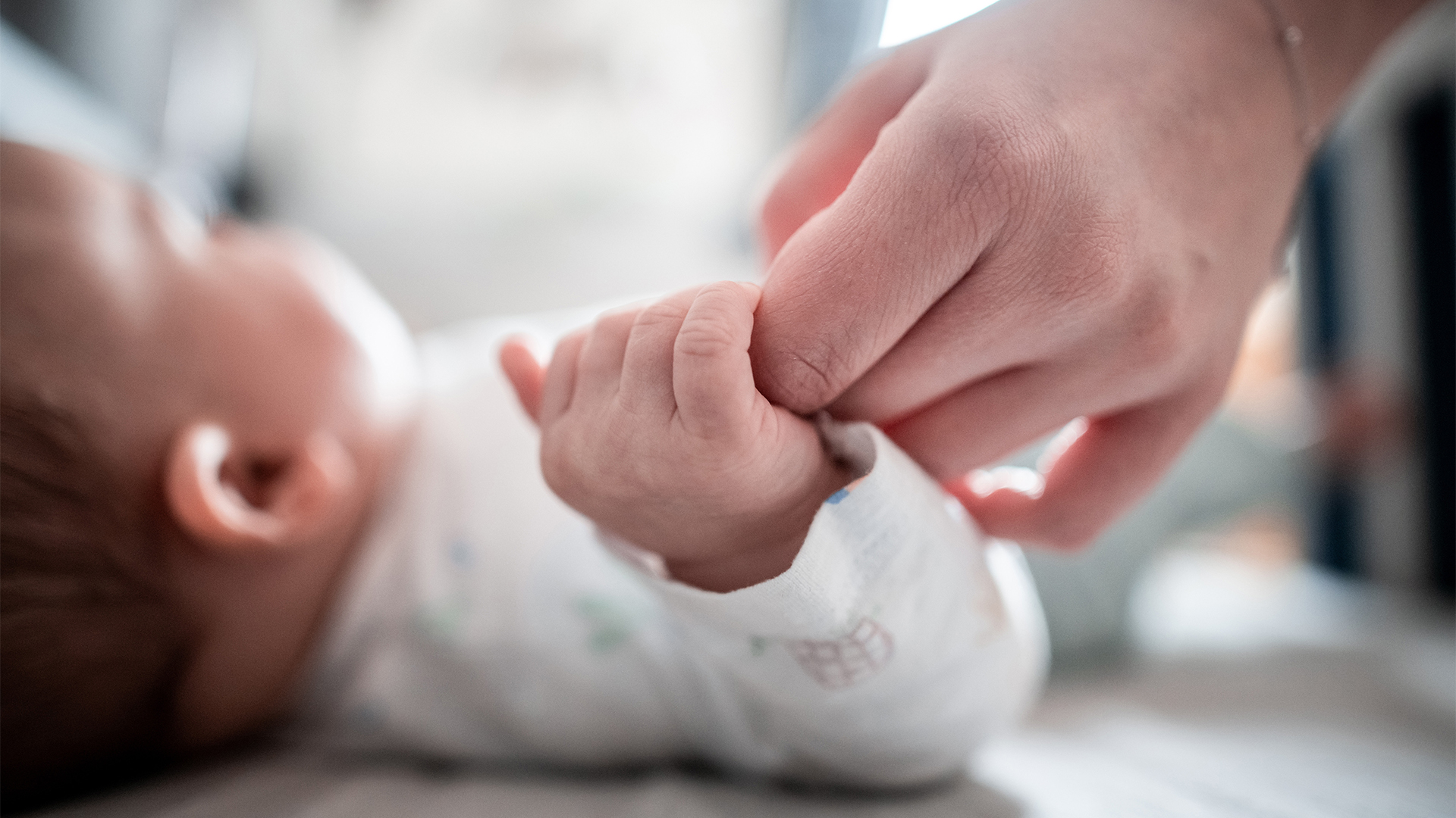 Ein Baby klammert sich an den Finger seiner Mutter | dpa