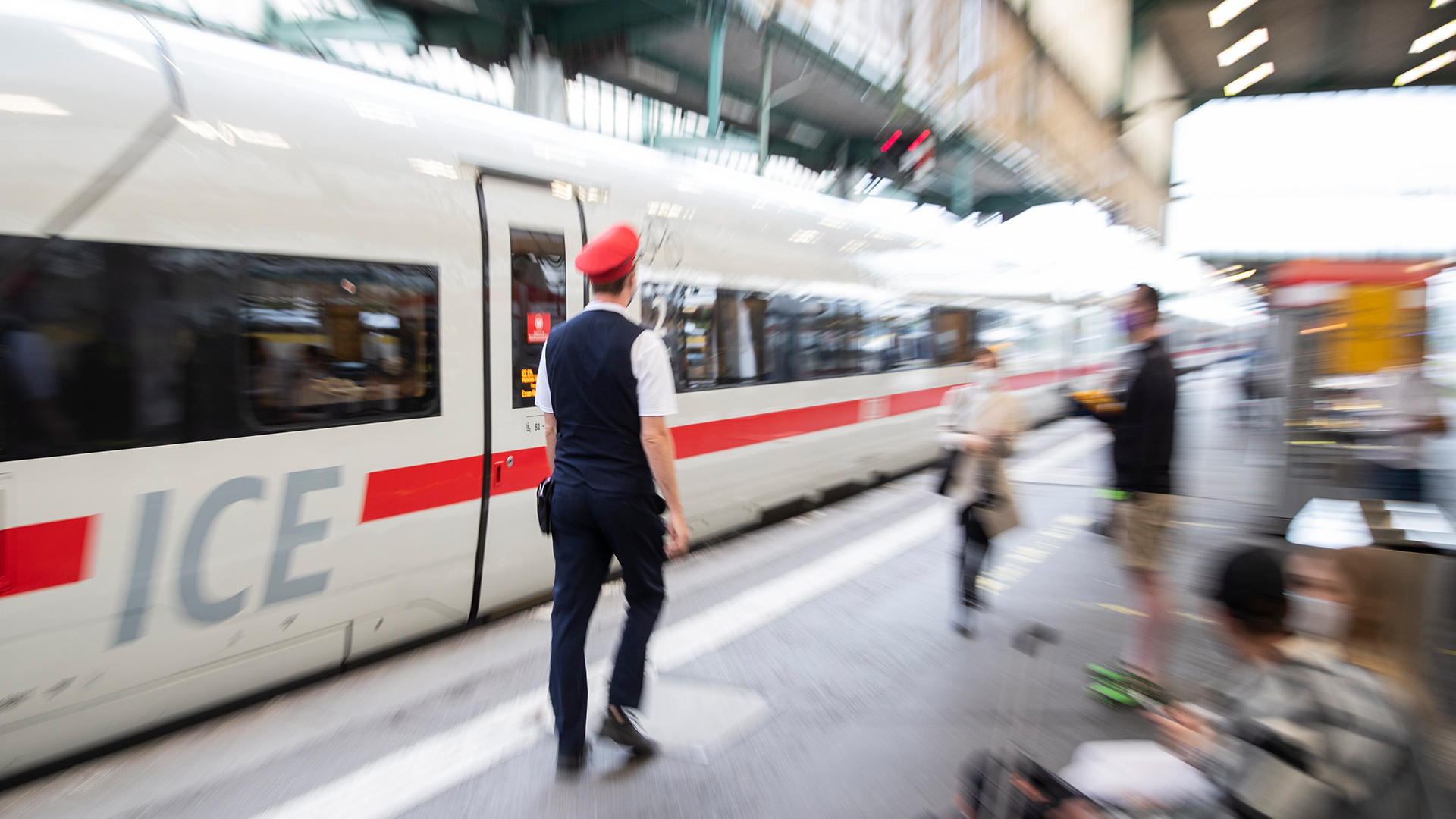Ein Mitarbeiter der Deutschen Bahn läuft an wartenden Reisenden vorbei, die vor einem ICE sitzen. | dpa