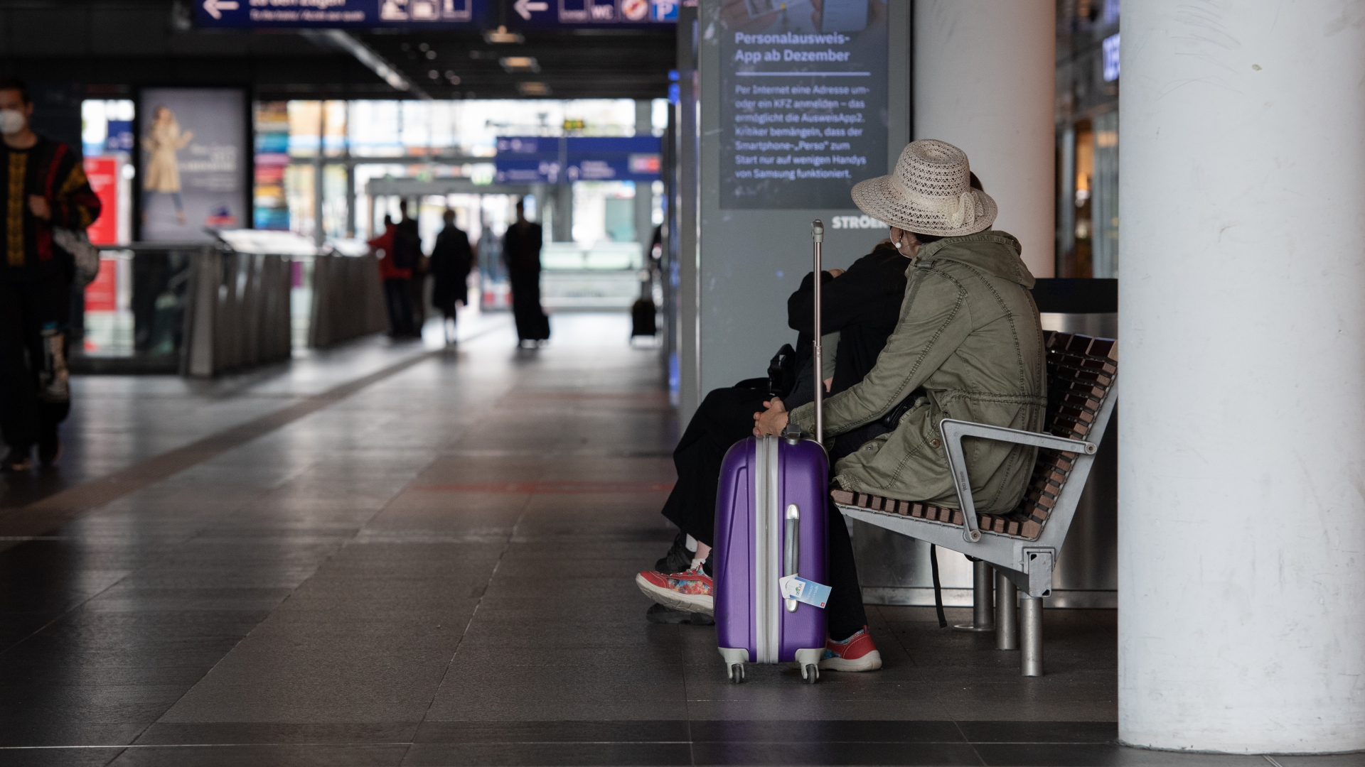 Eine Frau sitzt mit ihrem Koffer auf einer Bank im Hauptbahnhof in Berlin