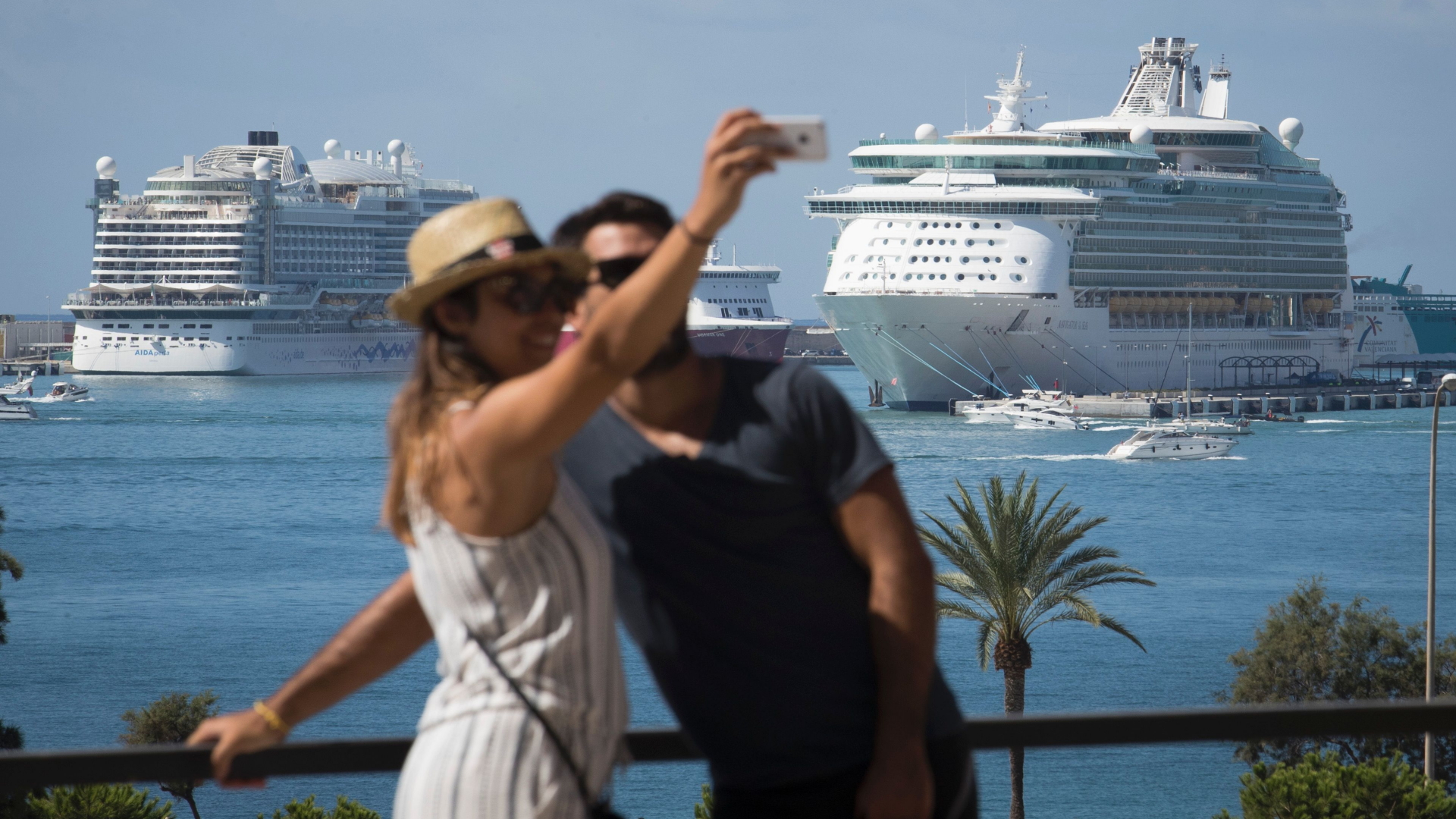Ein Paar schießt in Palma de Mallorca ein Foto, im Hintergrund zwei Kreuzfahrtschiffe. | AFP
