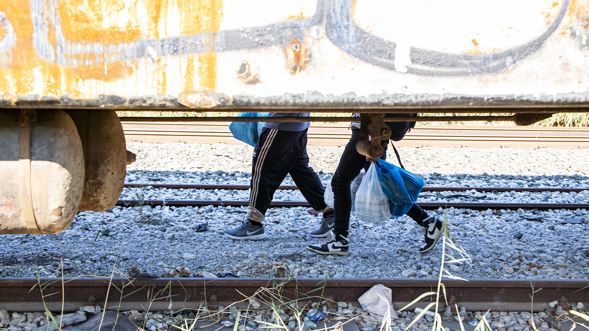 Zwei Menschen, von denen nur die Beine zu sehen sind, tragen Tüten über Gleise. | picture alliance / NurPhoto