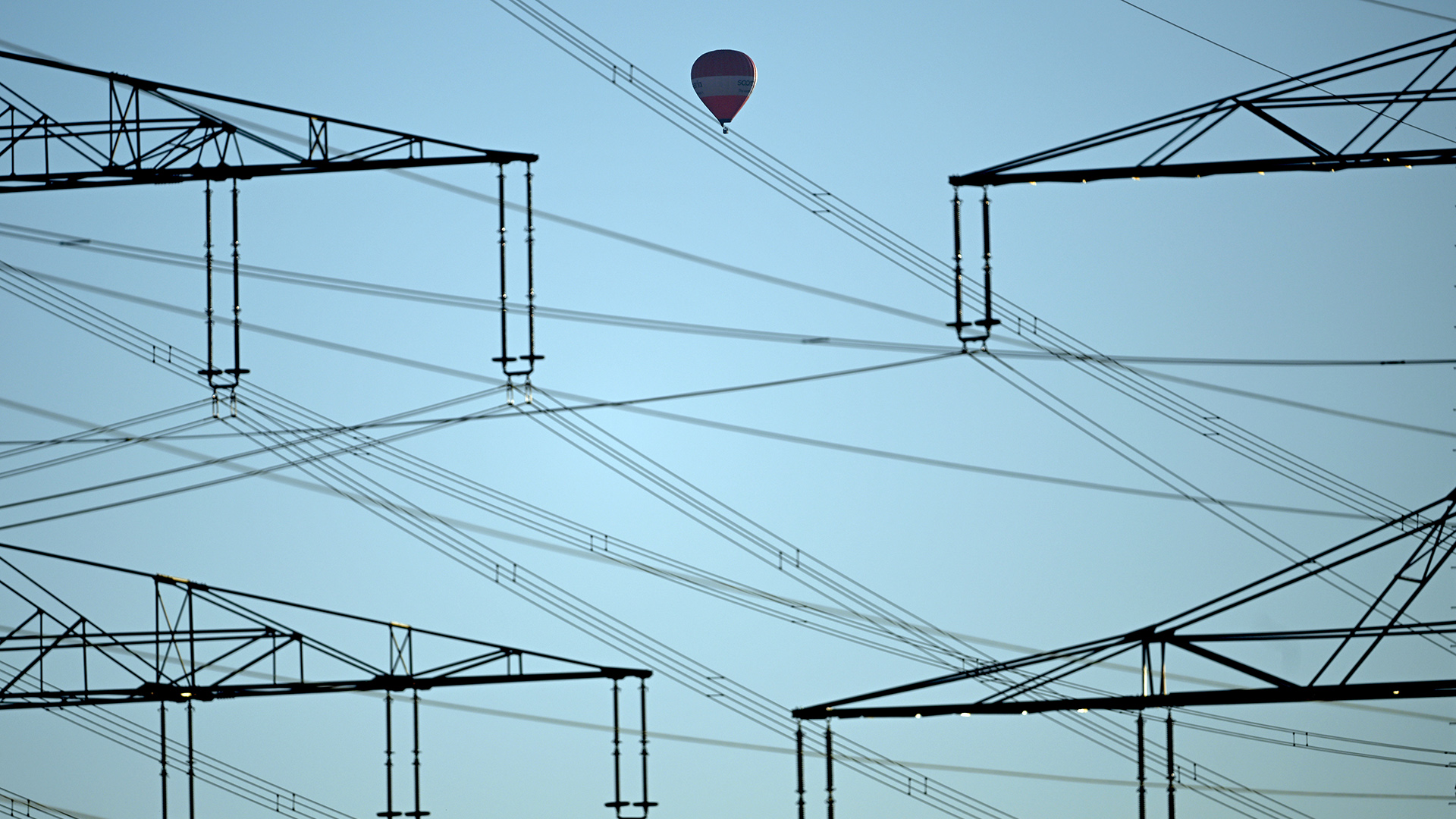 Hinter Strommasten fährt ein Heißluftballon vor blauem Himmel | dpa