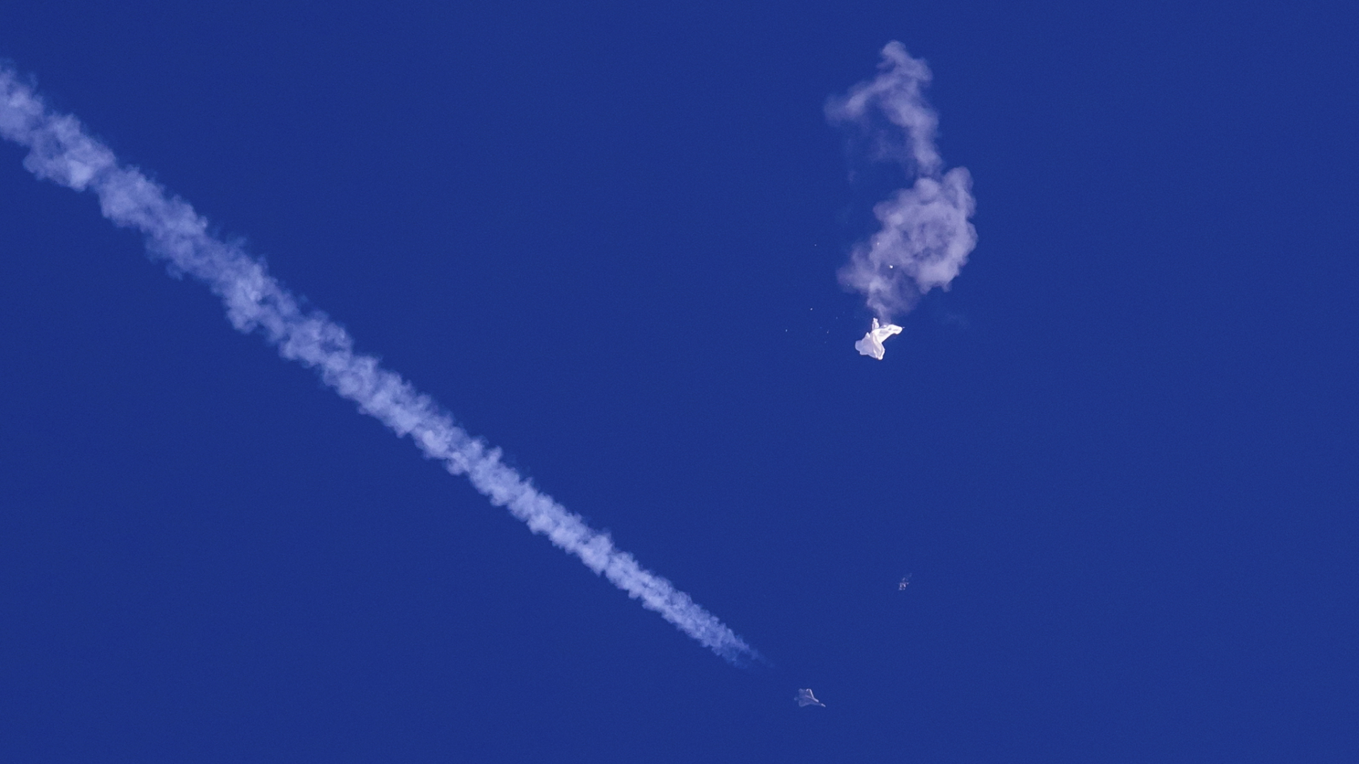 Die Überreste eines Ballons schweben in der Luft, darunter sind ein Kampfjet und seine Kondensstreifen zu sehen. (Aufnahme vom 4. Februar 2023) | dpa