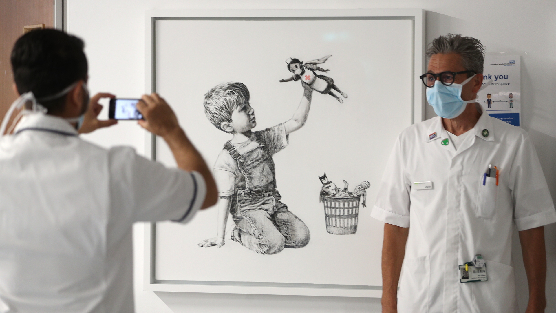 Großbritannien, Southampton: Ein medizinischer Mitarbeiter lässt sich vor dem Kunstwerk mit dem Titel "Game Changer" des Streetart-Künstlers Banksy fotografieren. | dpa