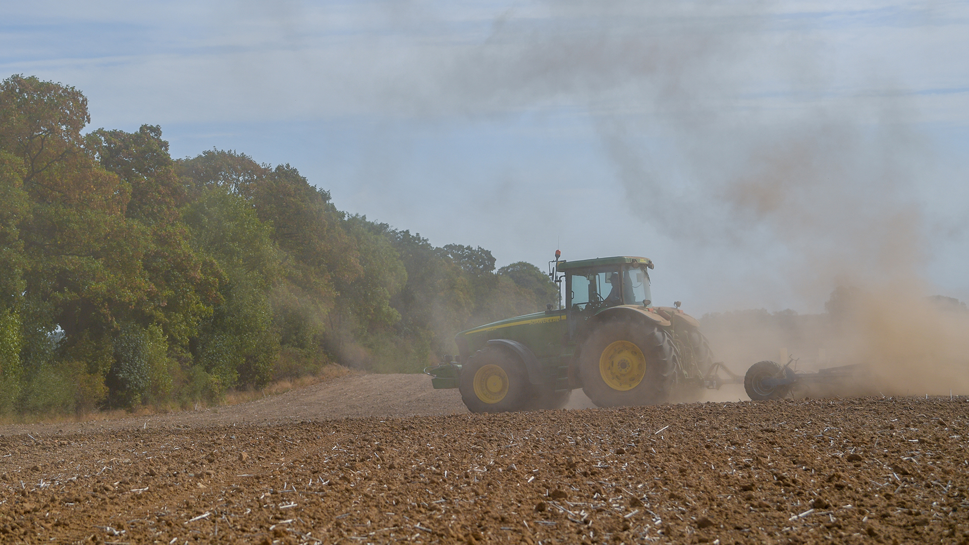Ein Landwirt bearbeitet mit Traktor und Grubber den Boden auf einem Acker in Brandenburg und wirbelt dabei viel Staub auf. | picture alliance/dpa